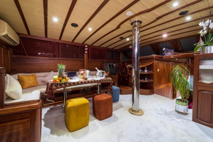 yacht interior salon with curved seating, exposed wooden beams, chrome pole and ottoman seating