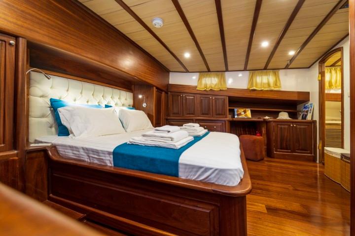 yacht guest cabin featuring double bed with white linens, blue accent pillows, wooden built-in furniture and shelving