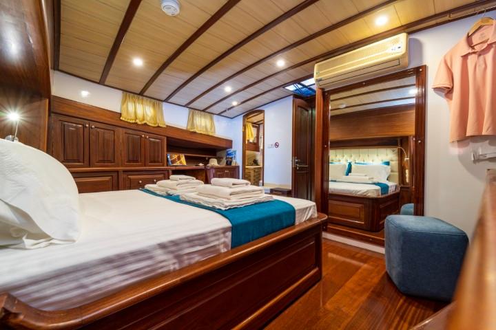 yacht cabin interior with double bed, dark wood built-in wardrobes and blue ottoman