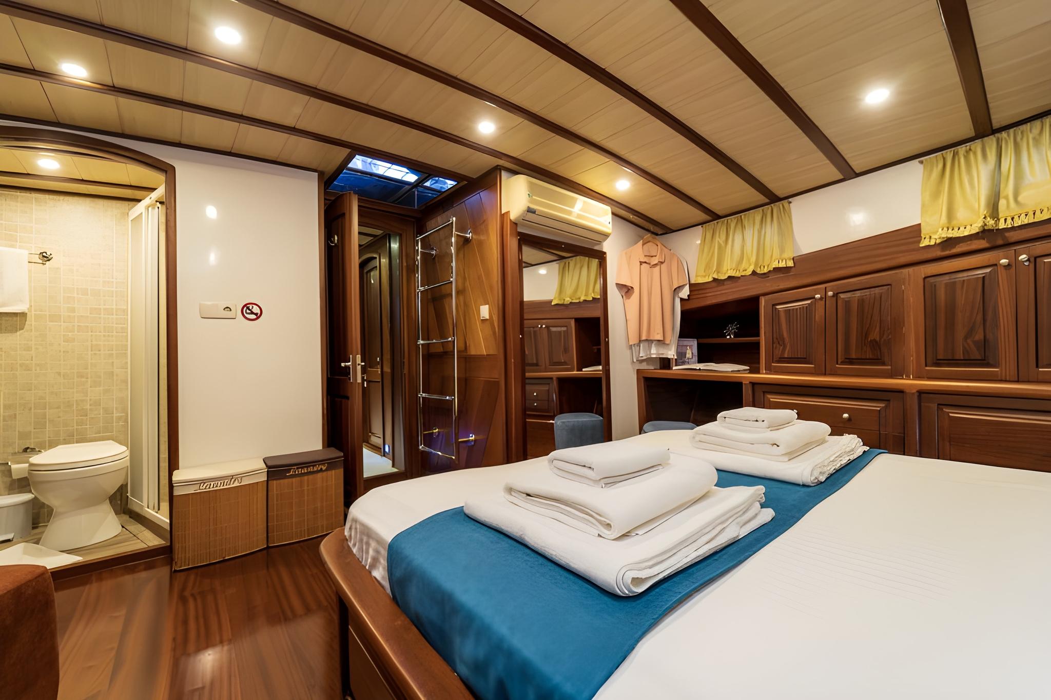 yacht cabin interior with white bedding, wooden paneling and en-suite bathroom with shower