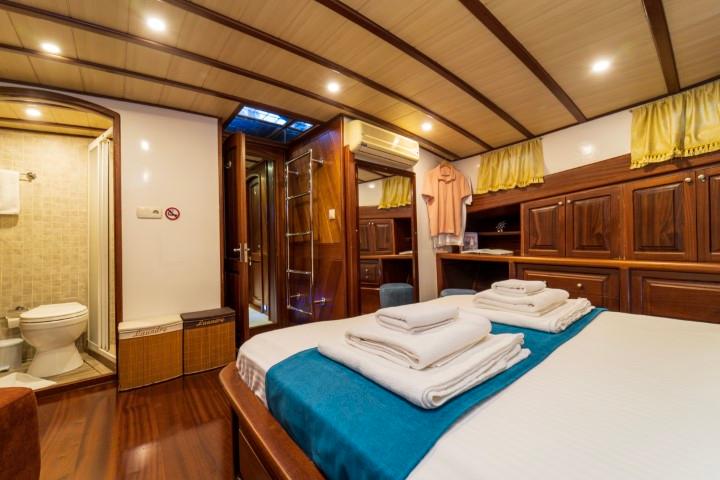 yacht cabin interior with white bedding, wooden paneling and en-suite bathroom with shower