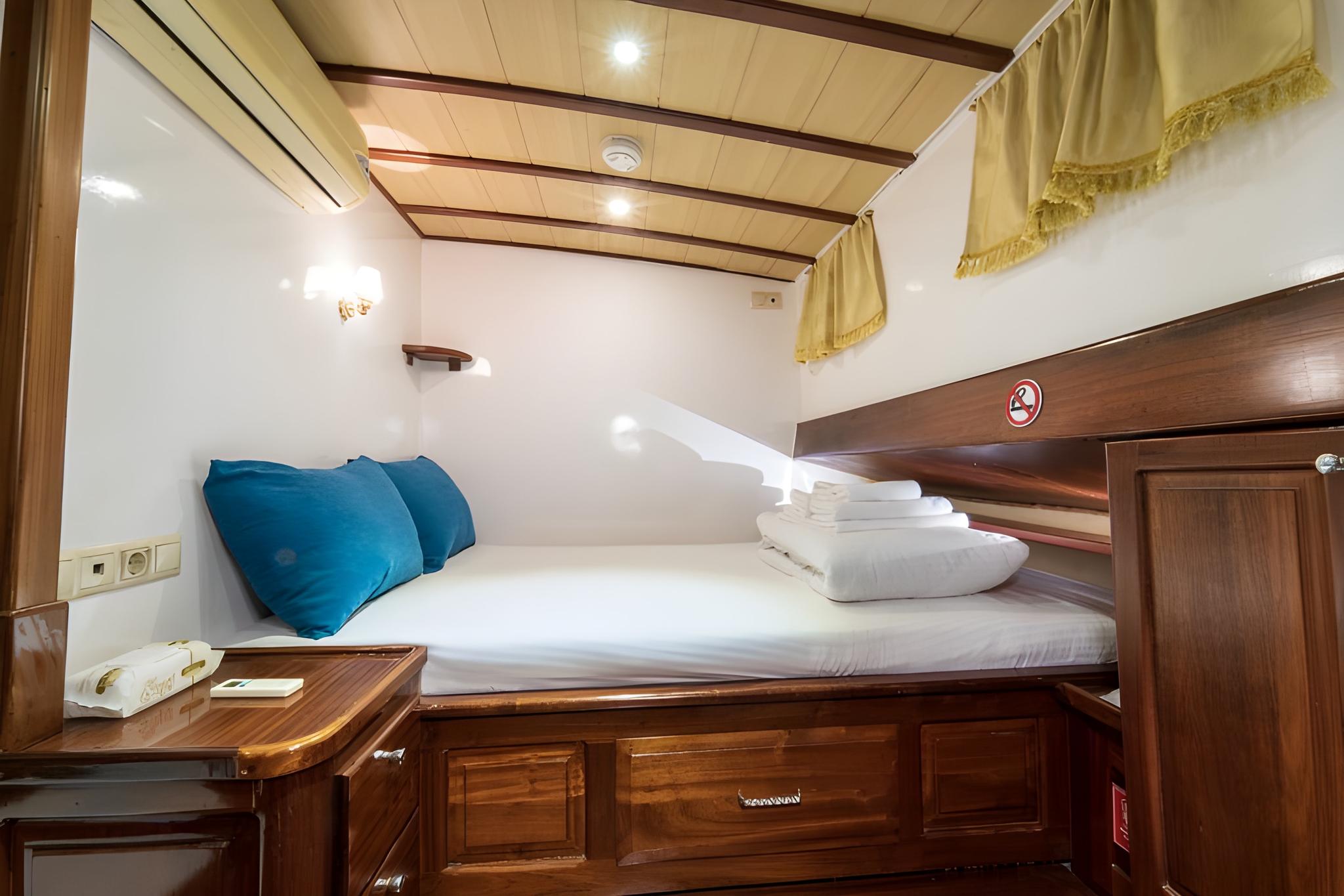 yacht cabin interior with single bed, blue pillows, built-in storage drawers and wood paneling