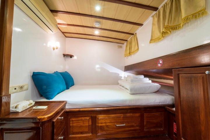 yacht cabin interior with single bed, blue pillows, built-in storage drawers and wood paneling