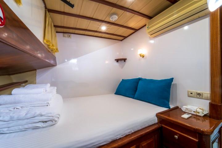 yacht cabin with white bedding, teal pillows, wooden ceiling beams and built-in storage