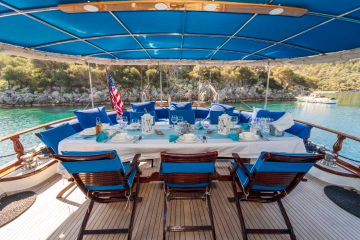aft deck dining table with white tablecloth and blue cushioned seating under bimini