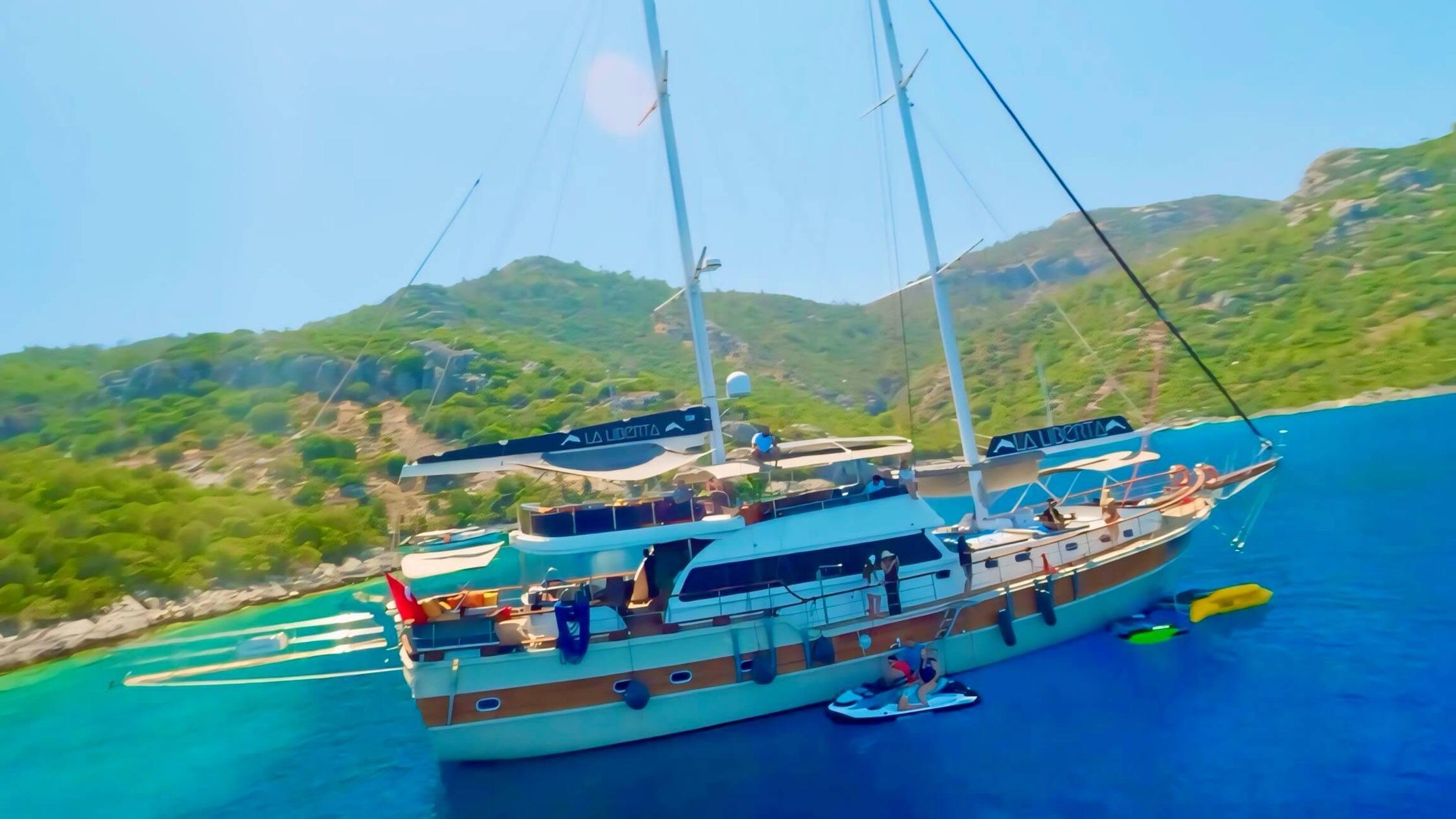 Aerial drone view of gulet La Liberta anchored in turquoise bay with jet ski and water toys alongside