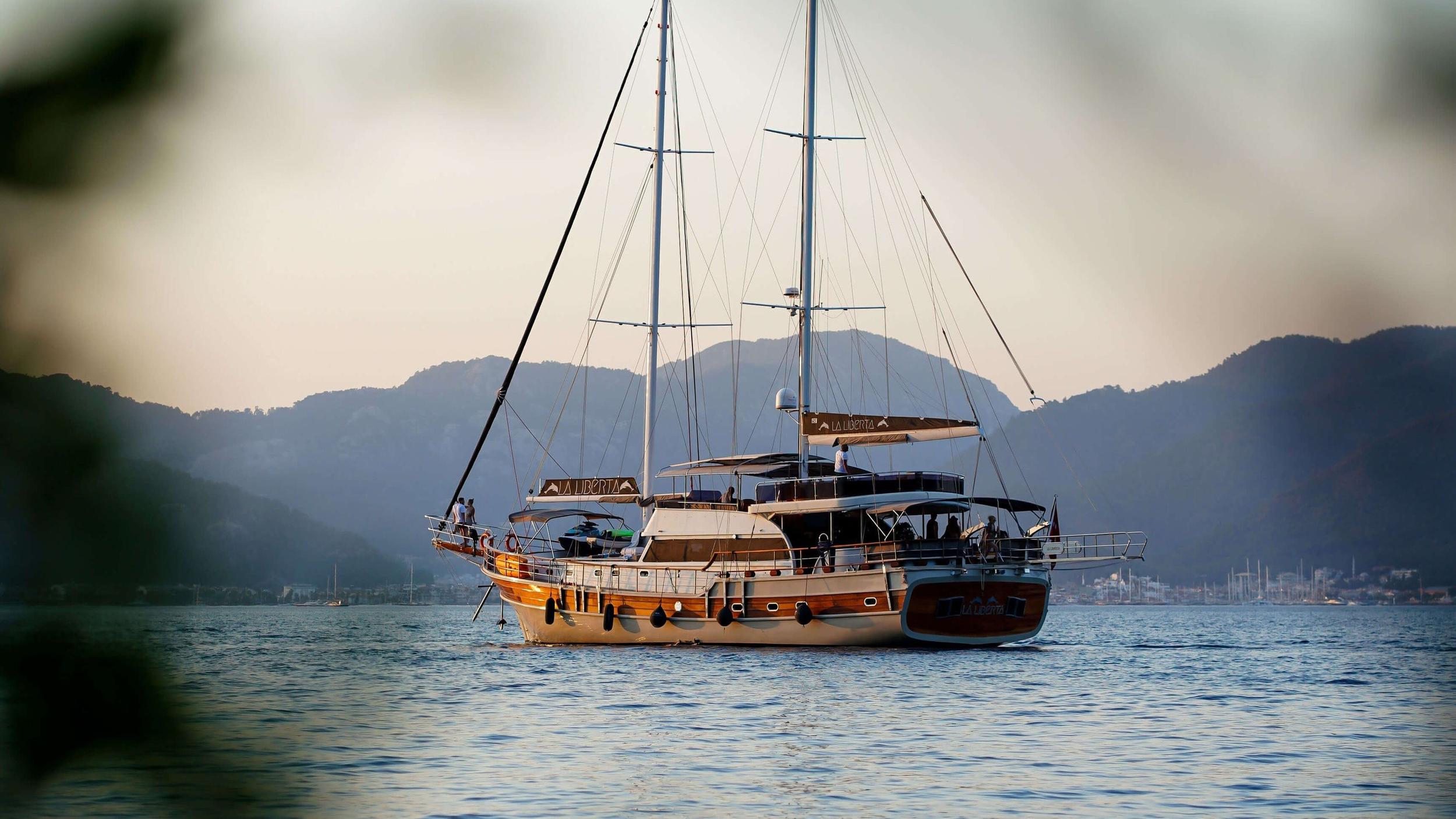 Luxury gulet La Liberta anchored in calm bay with hazy mountain backdrop at golden hour