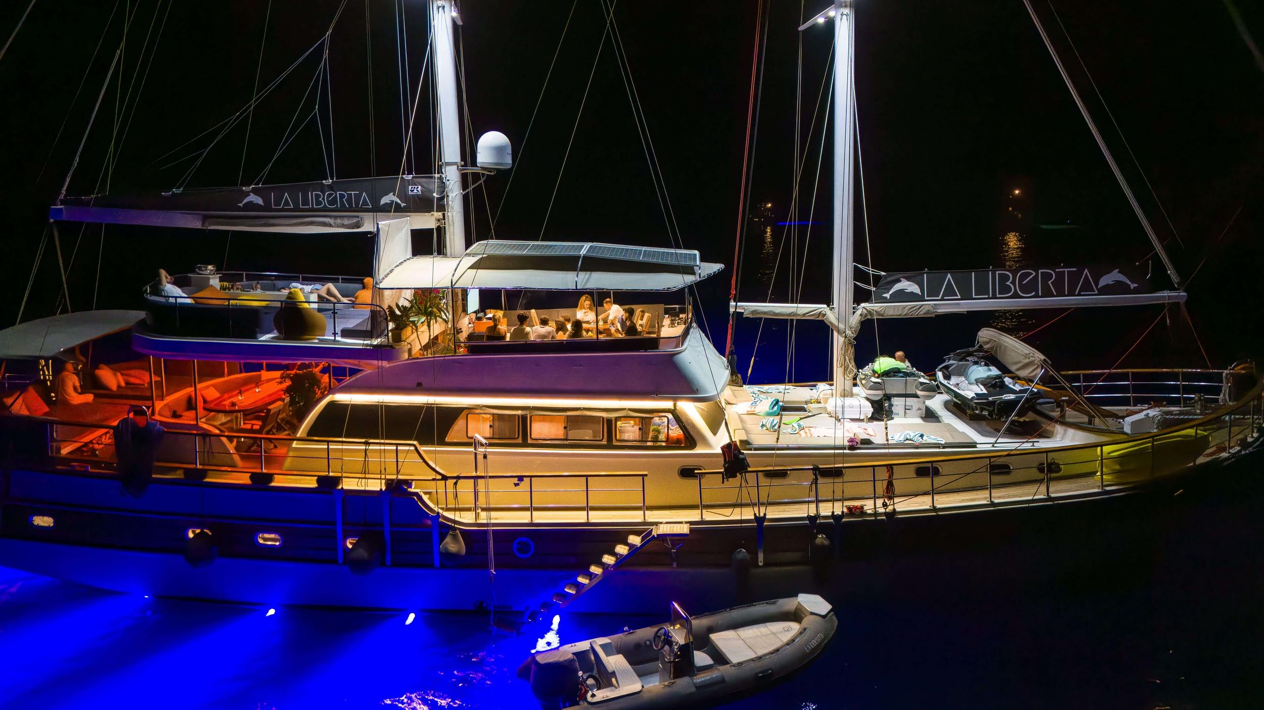 Aerial night shot of gulet La Liberta with guests dining on deck, jet ski, and tender alongside