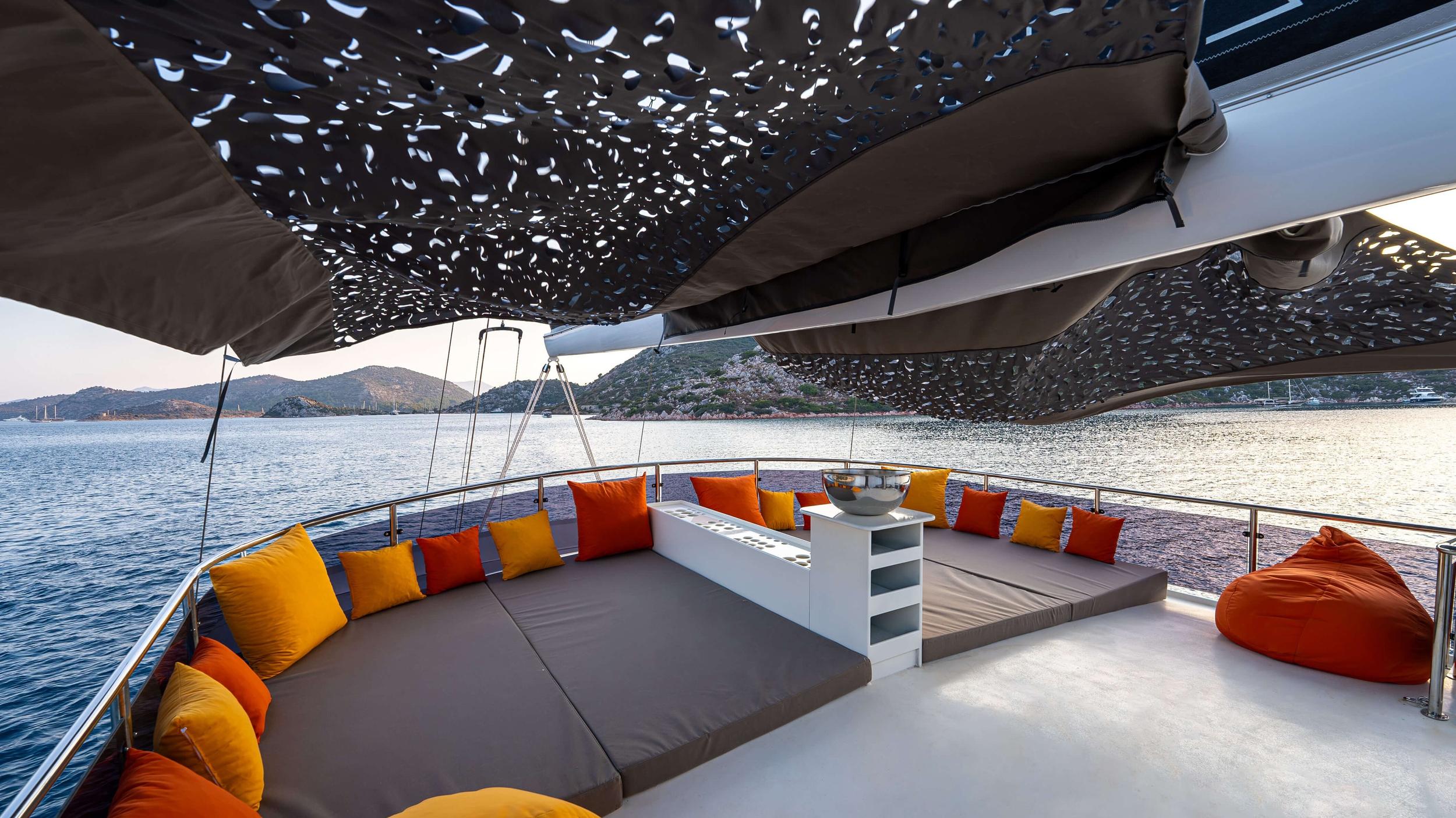 gulet bow deck curved grey sofa with orange and yellow cushions under laser-cut shade canopy