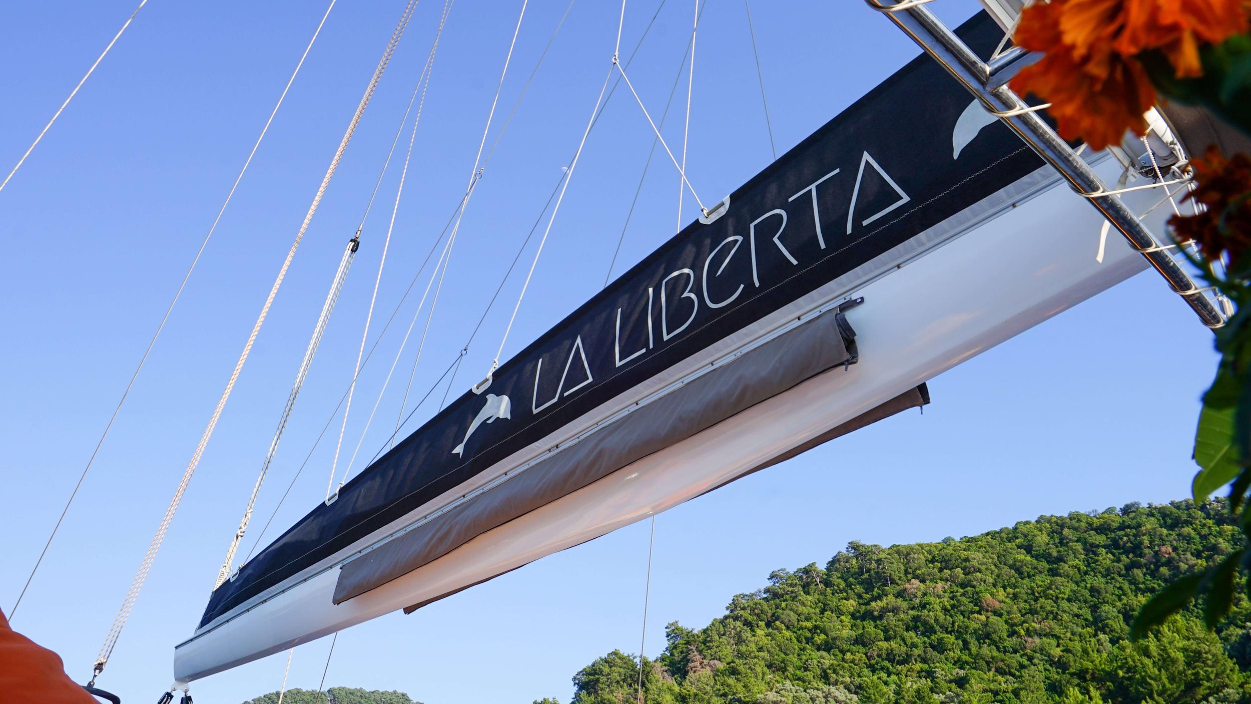 La Liberta gulet yacht boom with black mainsail cover and vessel name lettering against clear blue sky