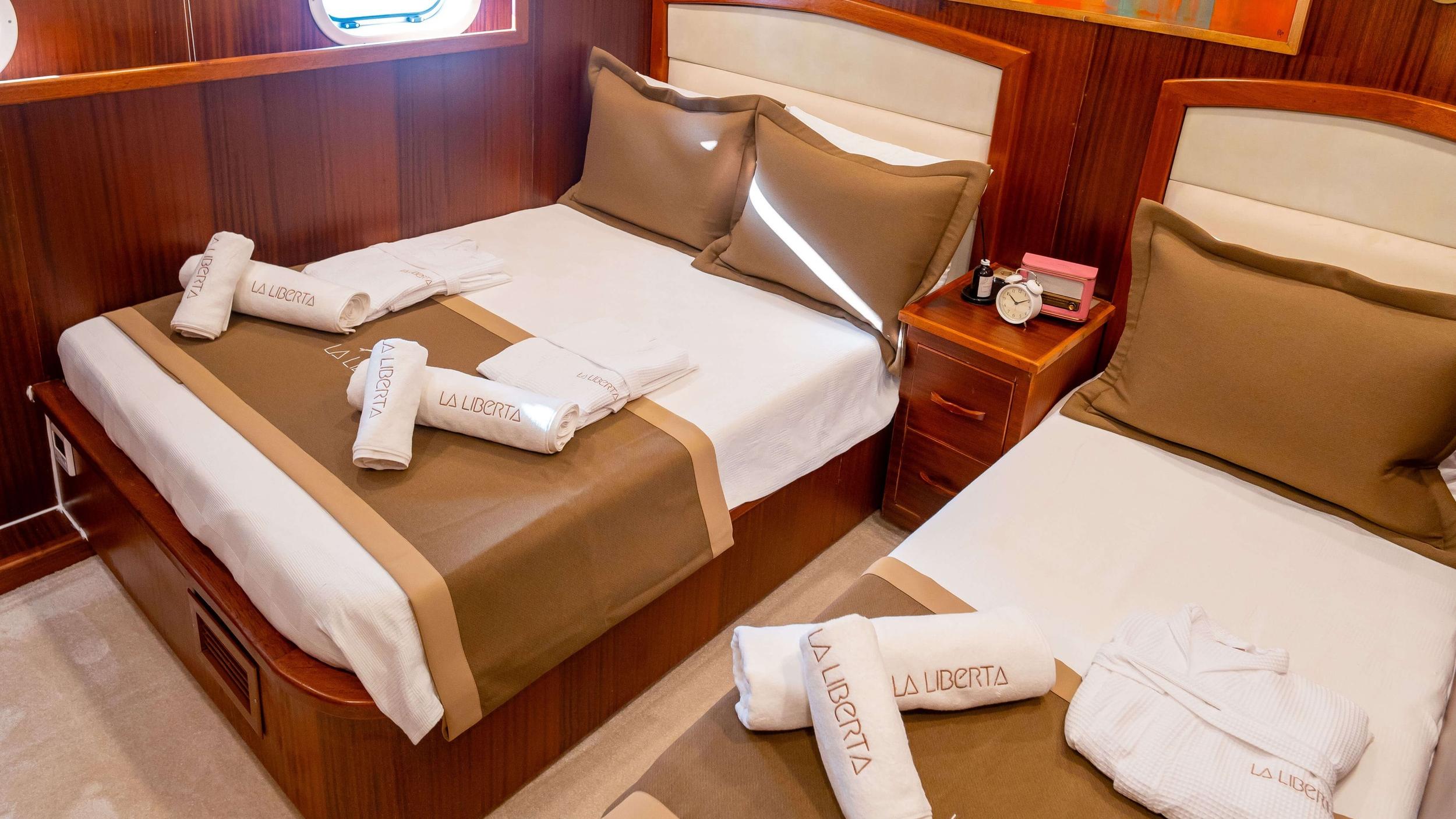 La Liberta gulet twin cabin with two beds, branded robes and towels, wooden panelling and porthole
