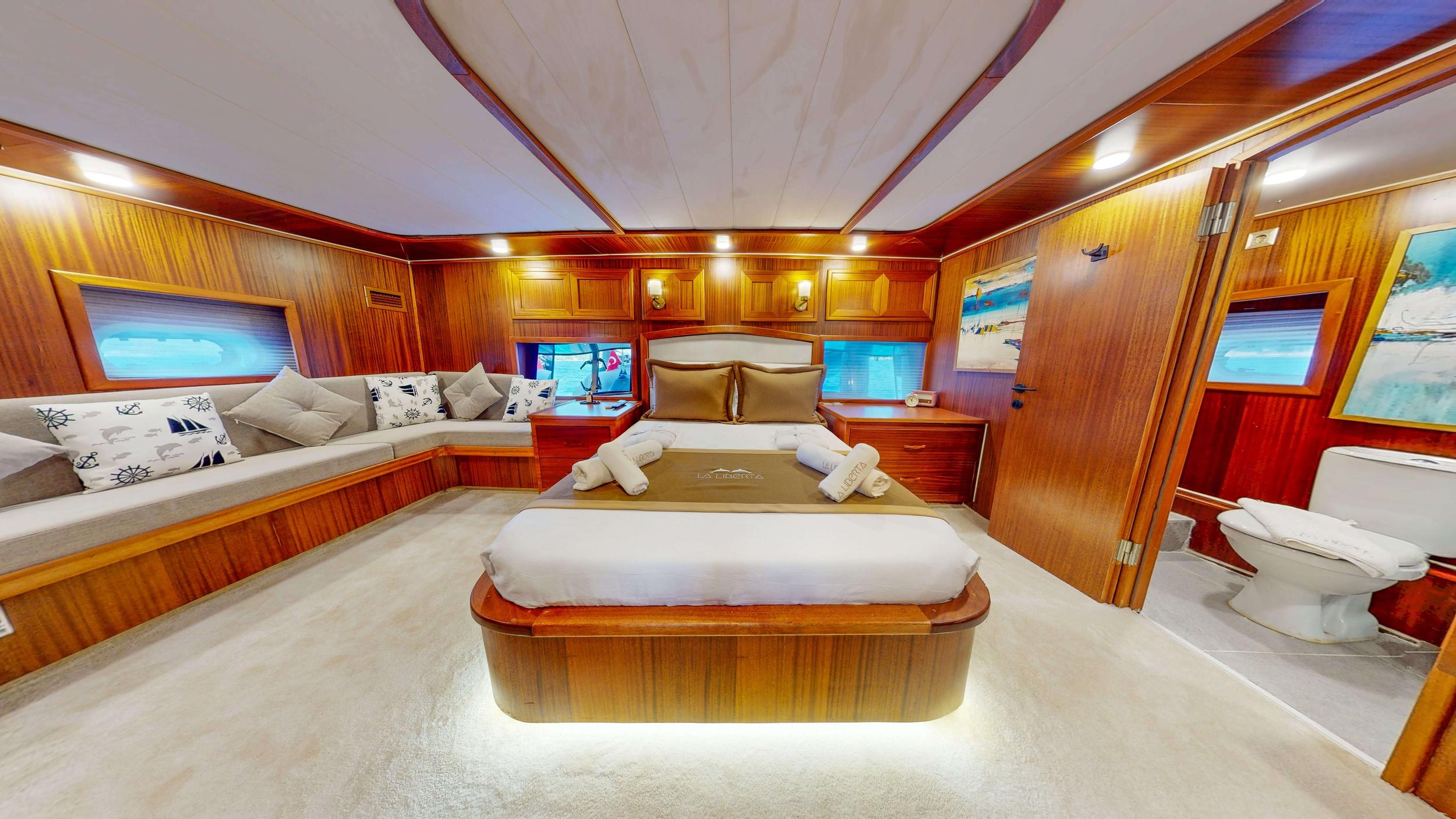 Gulet master cabin with illuminated king bed, L-shaped sofa seating and en-suite toilet visible
