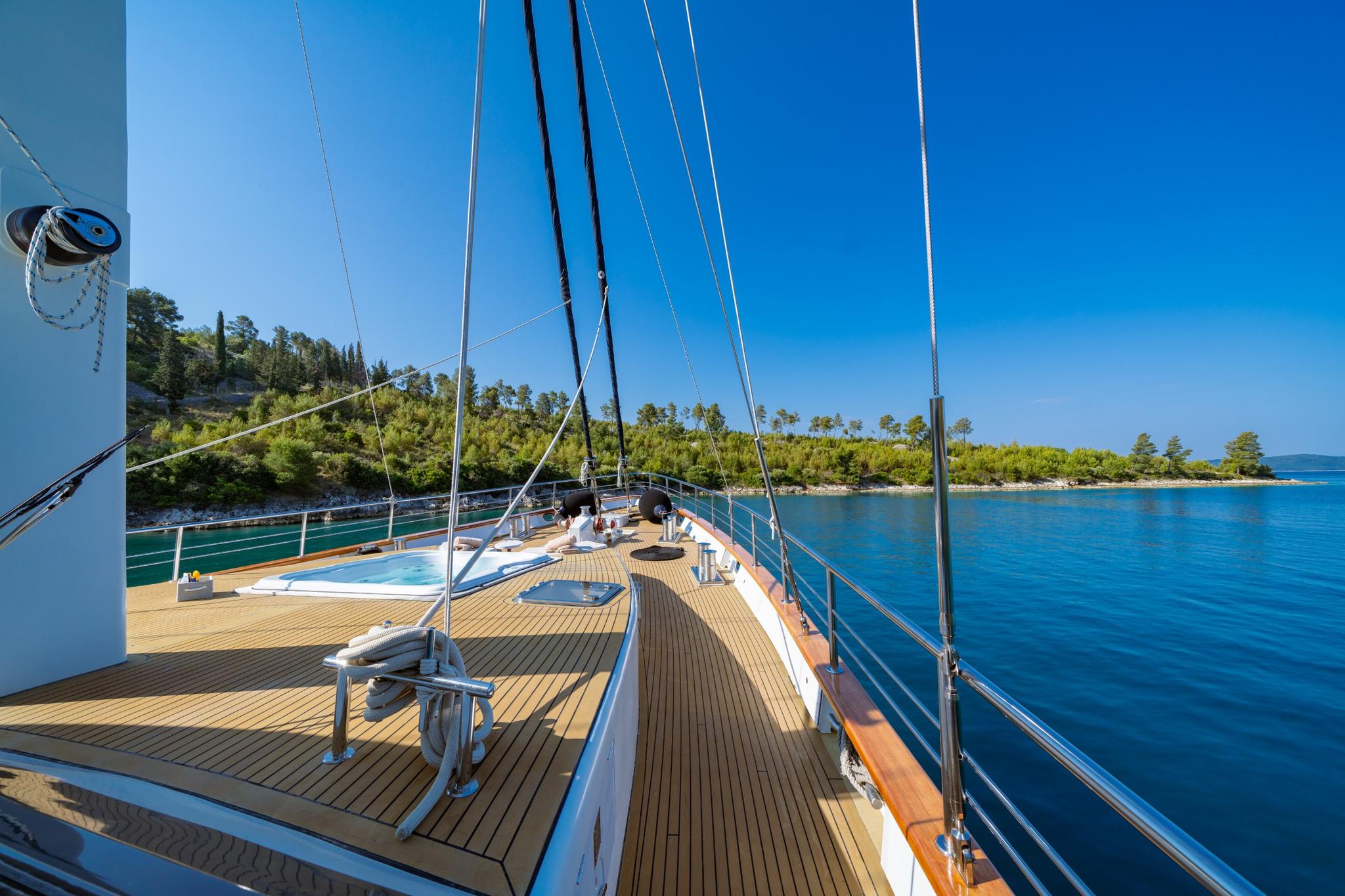 Gulet foredeck with teak planking, stainless steel rigging and anchor windlass overlooking Mediterranean coastline