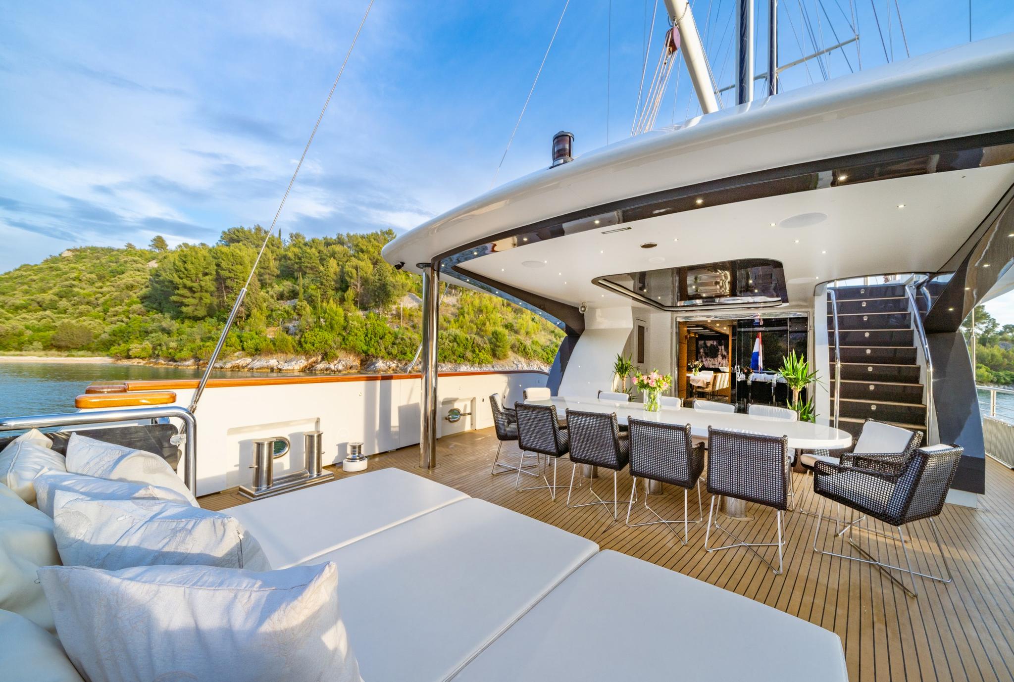luxury yacht aft deck with outdoor dining table, wicker chairs and white cushioned seating