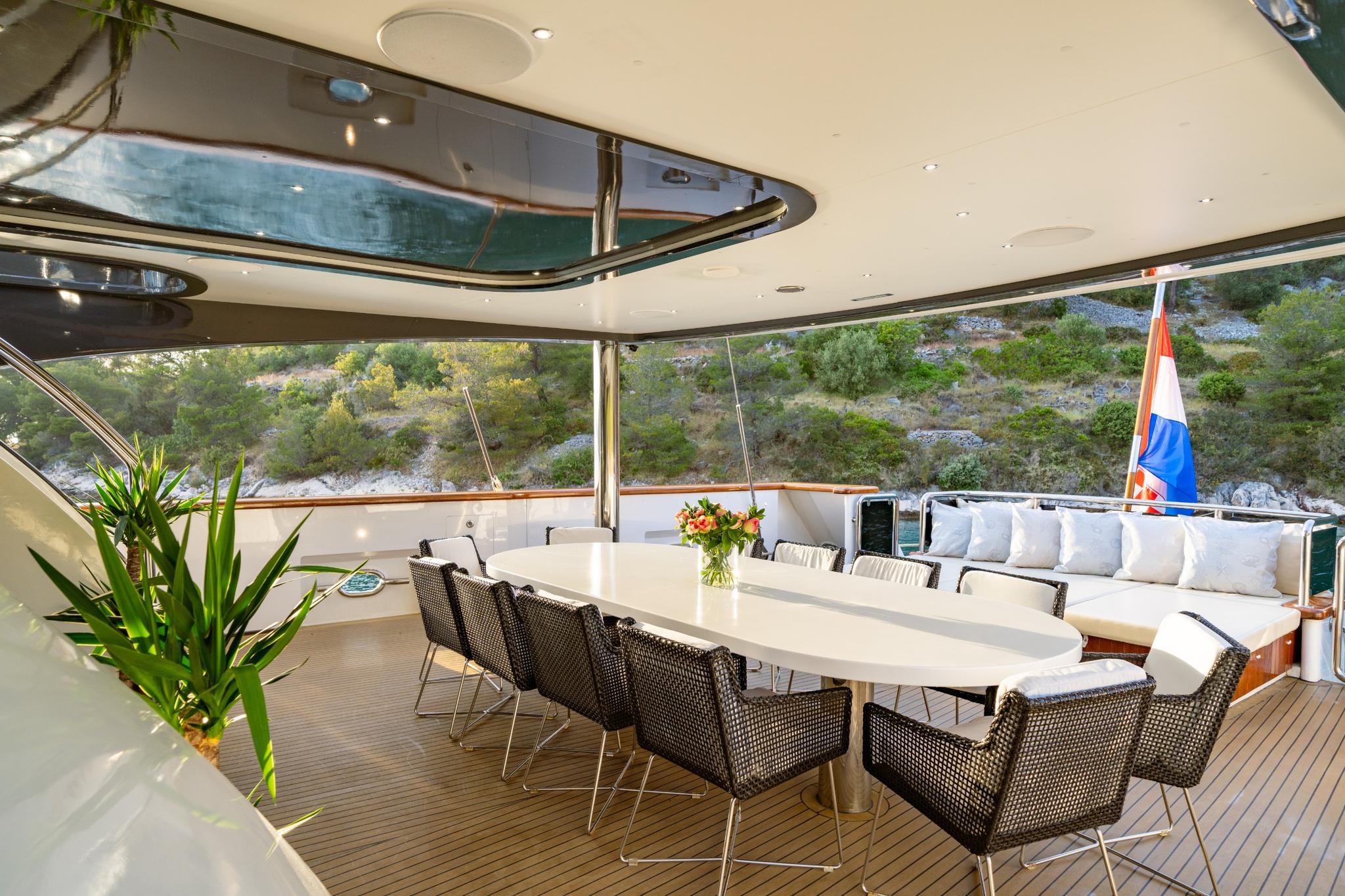 luxury yacht covered aft deck with white dining table, wicker chairs and built-in seating
