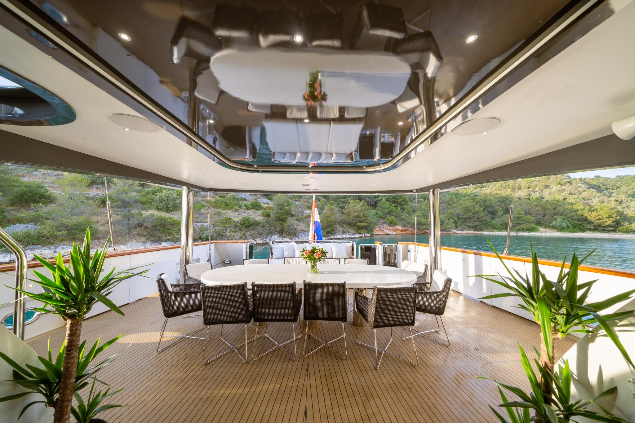 yacht aft deck dining area with white table, wicker chairs under hardtop canopy