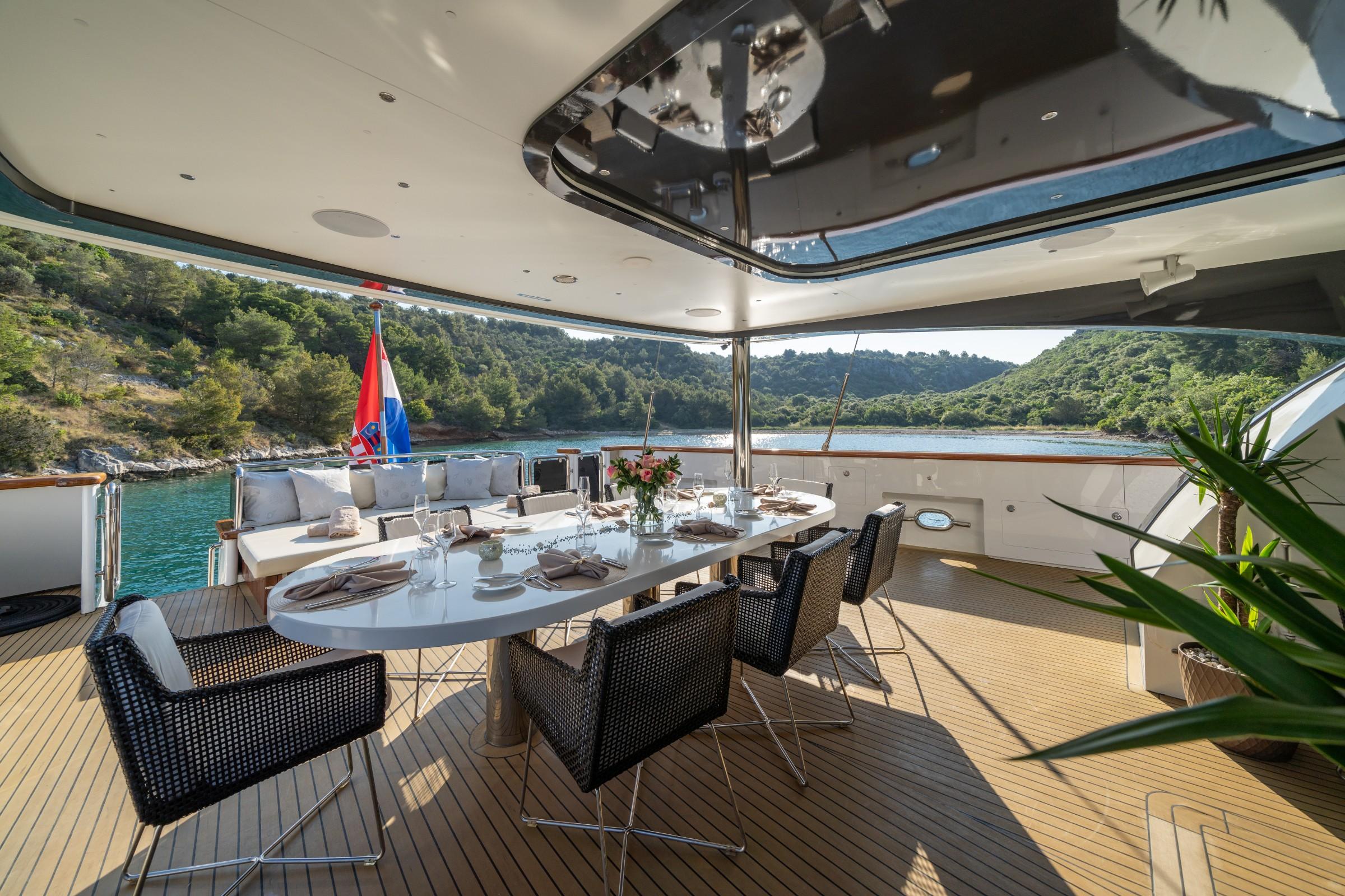 yacht aft deck dining area with white table, wicker chairs, and panoramic windows