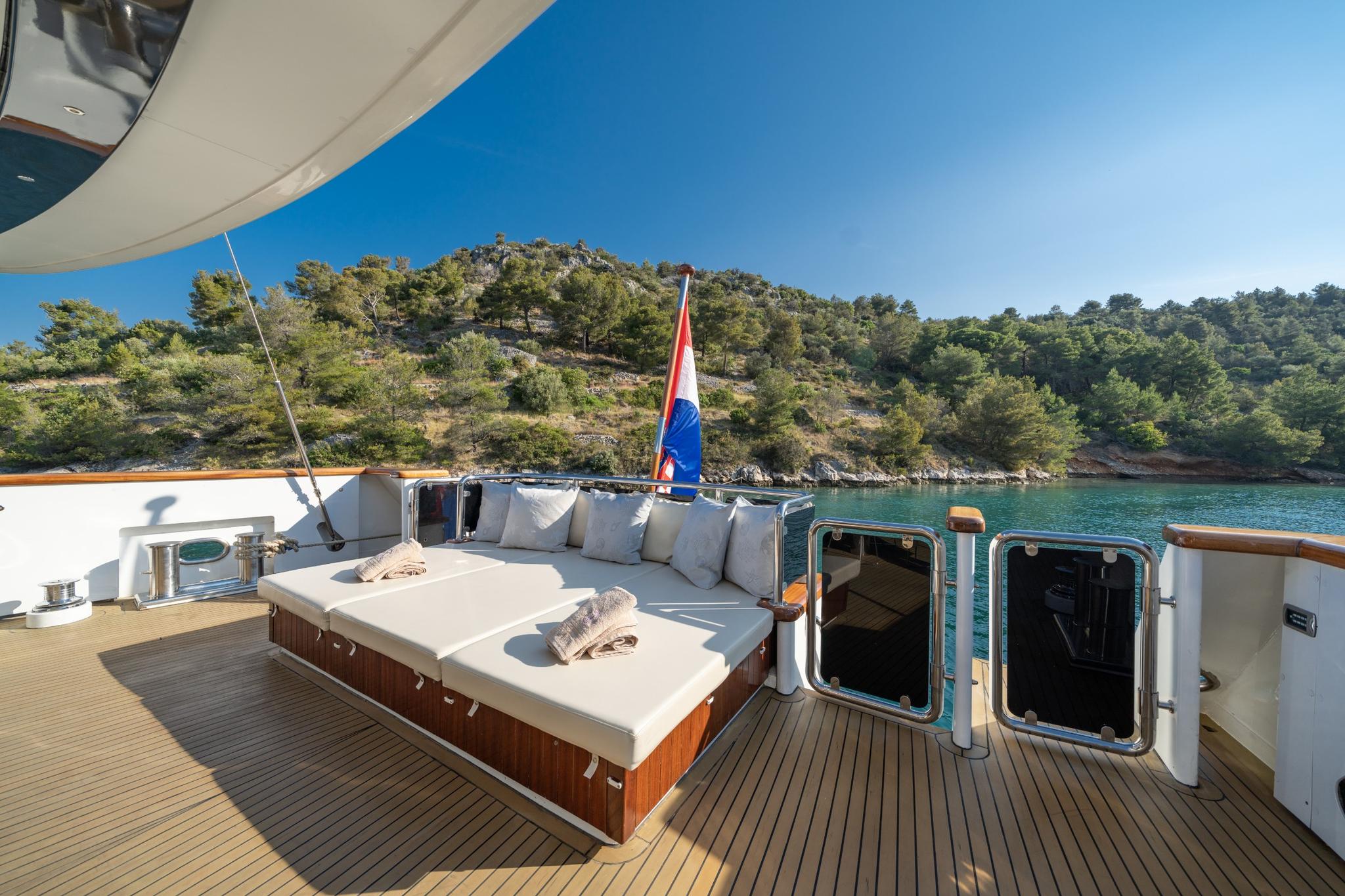 yacht aft deck with white cushioned seating area and teak decking overlooking turquoise bay