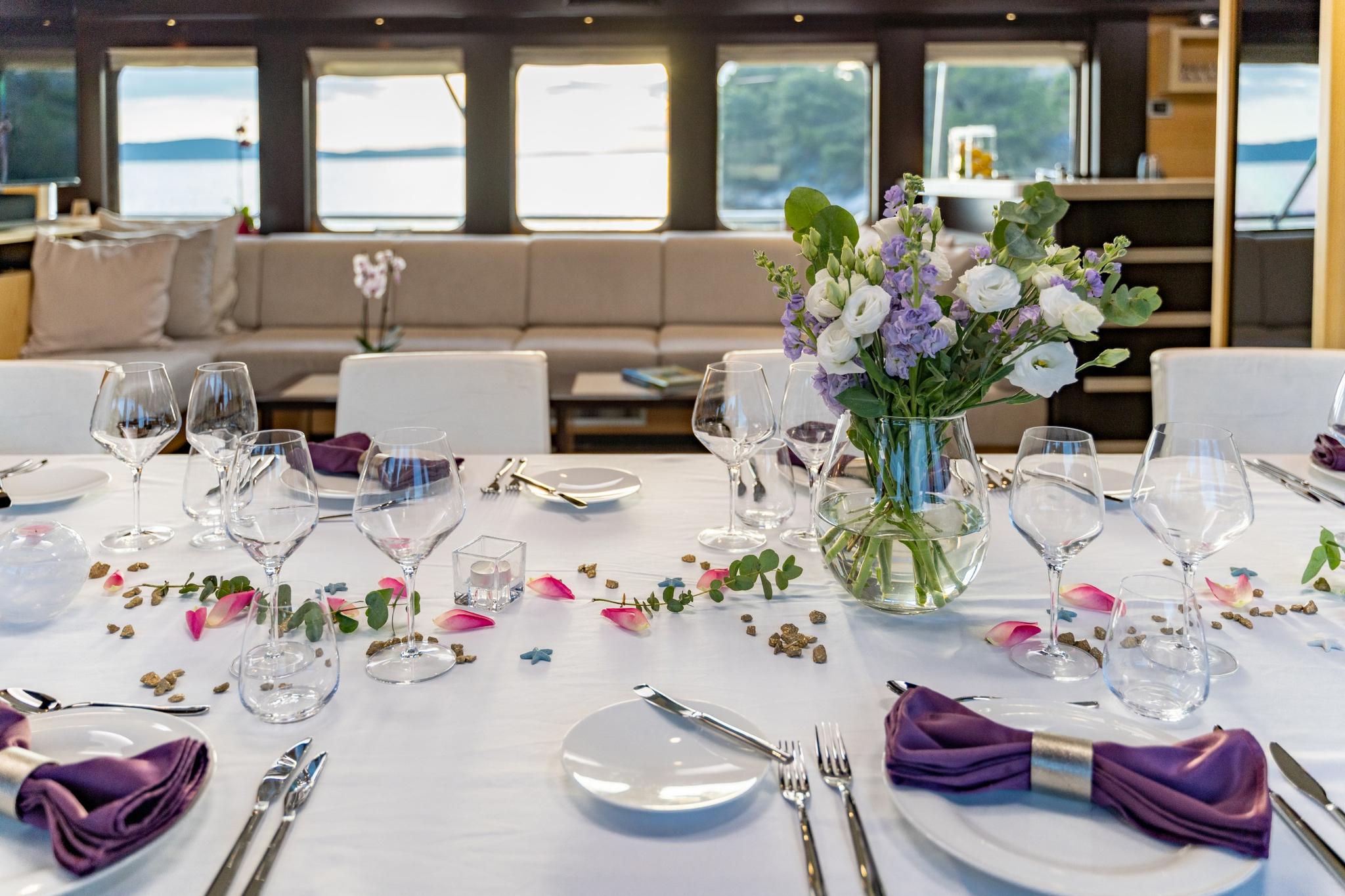 elegant yacht dining table set with wine glasses, purple napkins and white flower arrangement