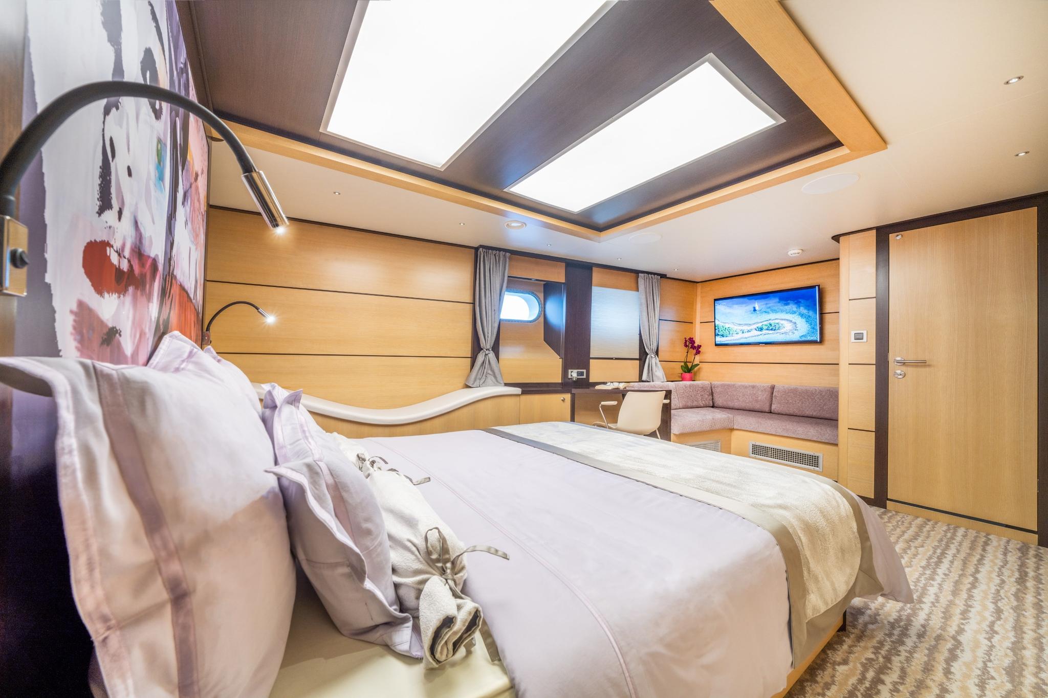 luxury yacht master cabin with king bed, overhead skylight, wall-mounted TV and seating area