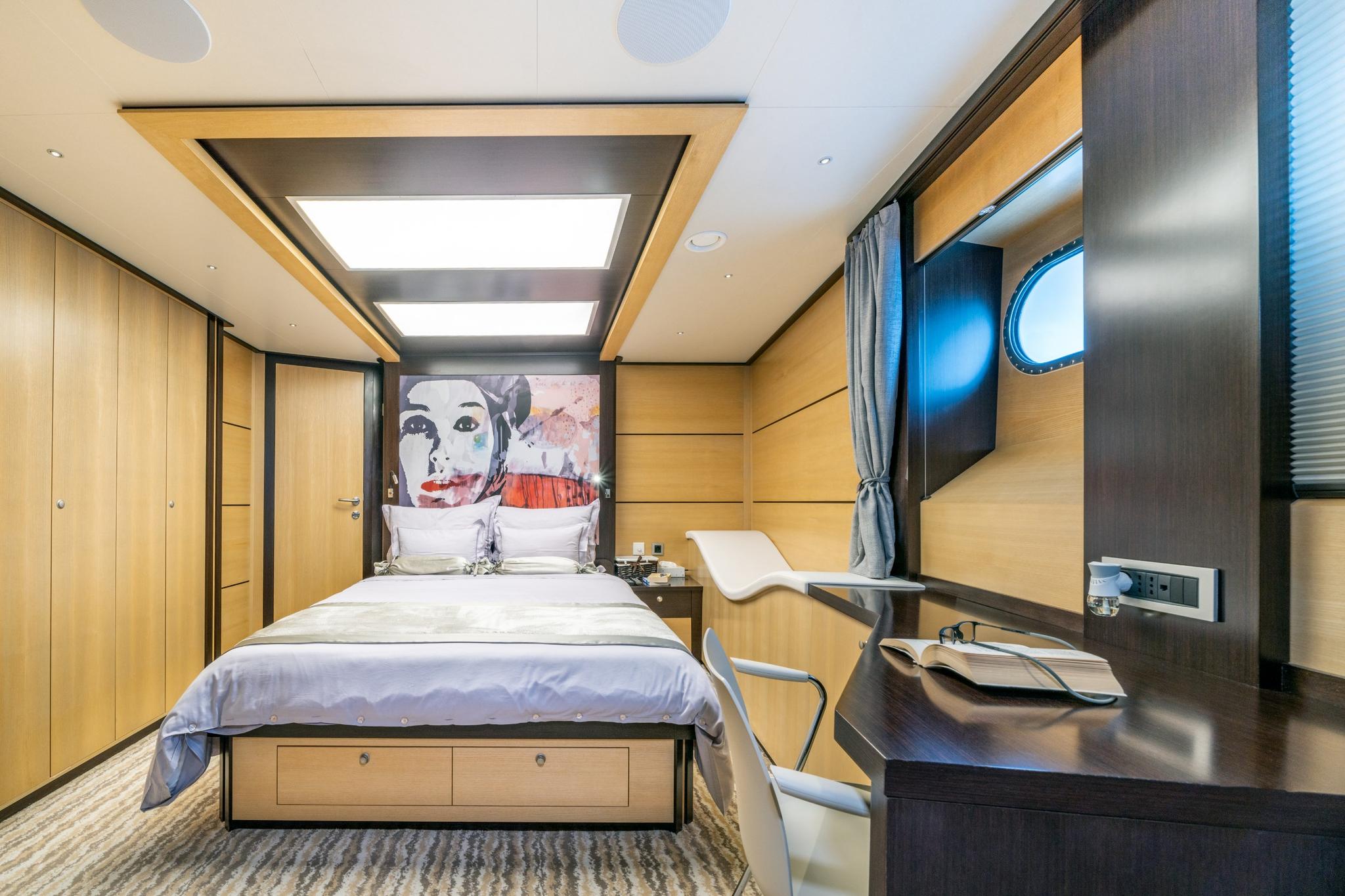 yacht guest cabin featuring double bed with storage drawers, built-in desk, and porthole windows