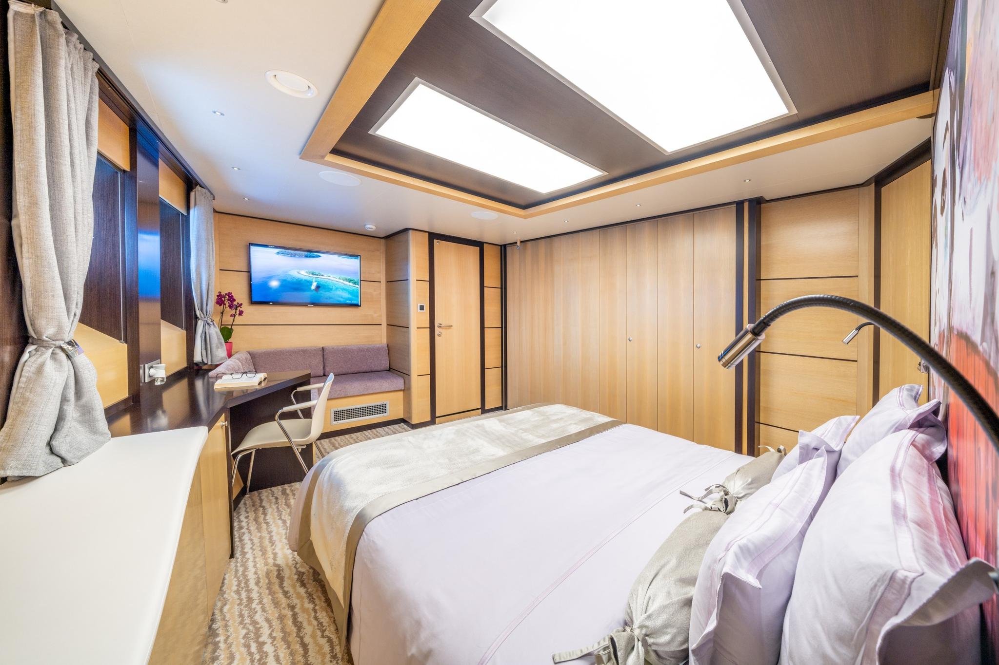 yacht cabin interior with double bed, wall-mounted television, and light wood paneling