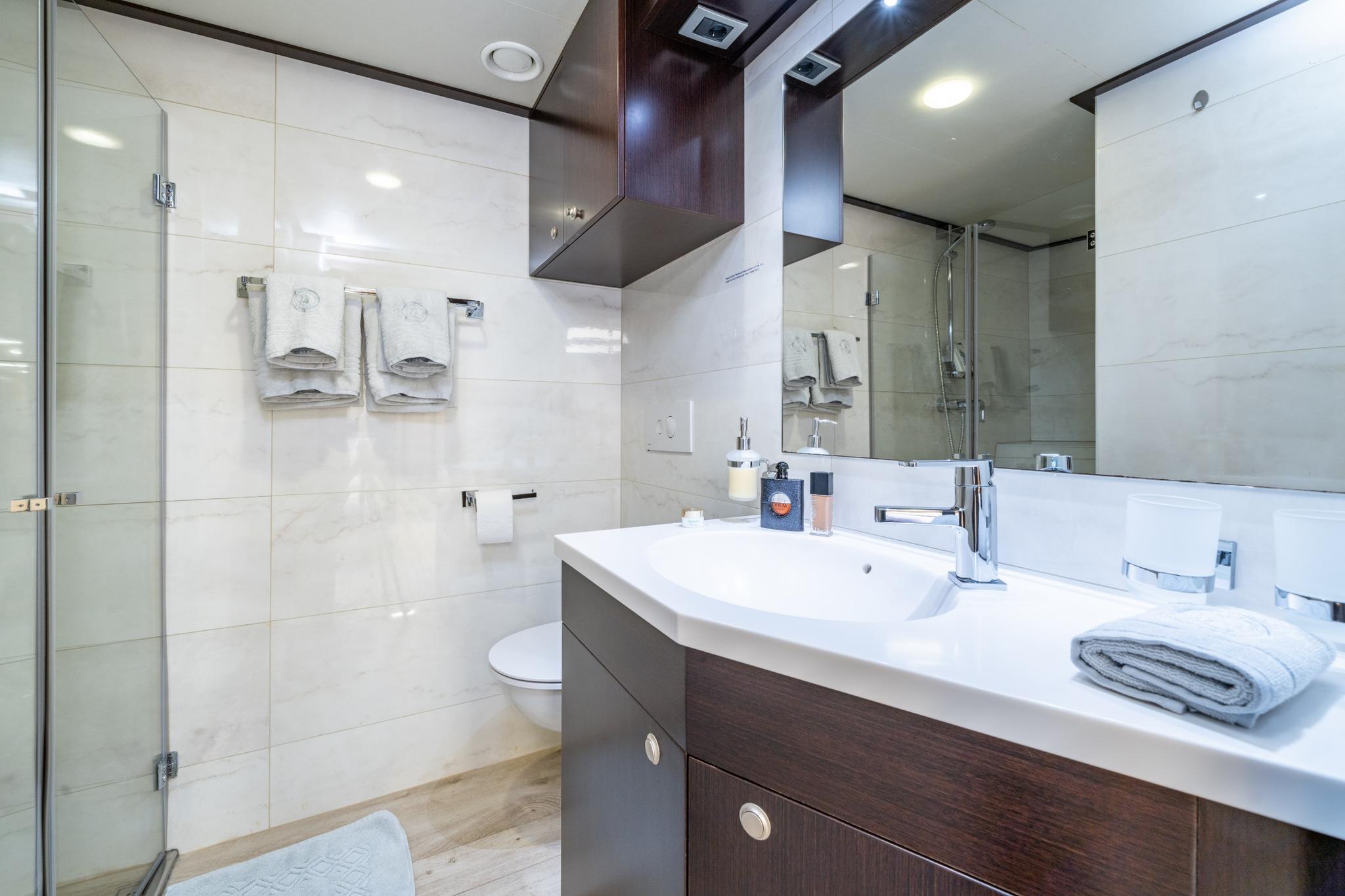 modern yacht bathroom featuring white vanity, large mirror, glass shower enclosure and marble surfaces