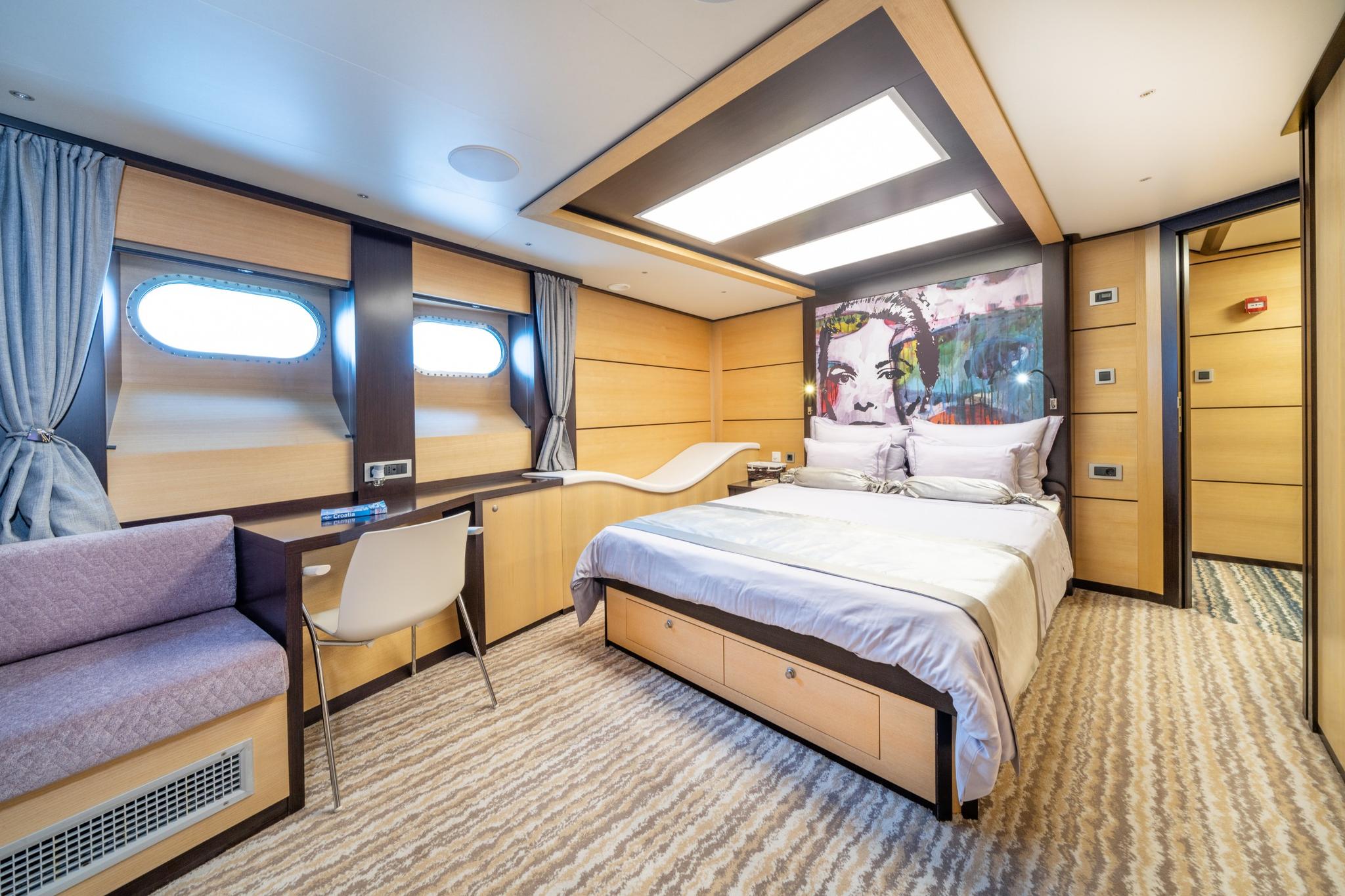 yacht guest cabin featuring double bed with storage drawers, built-in desk, sofa seating and oval portholes