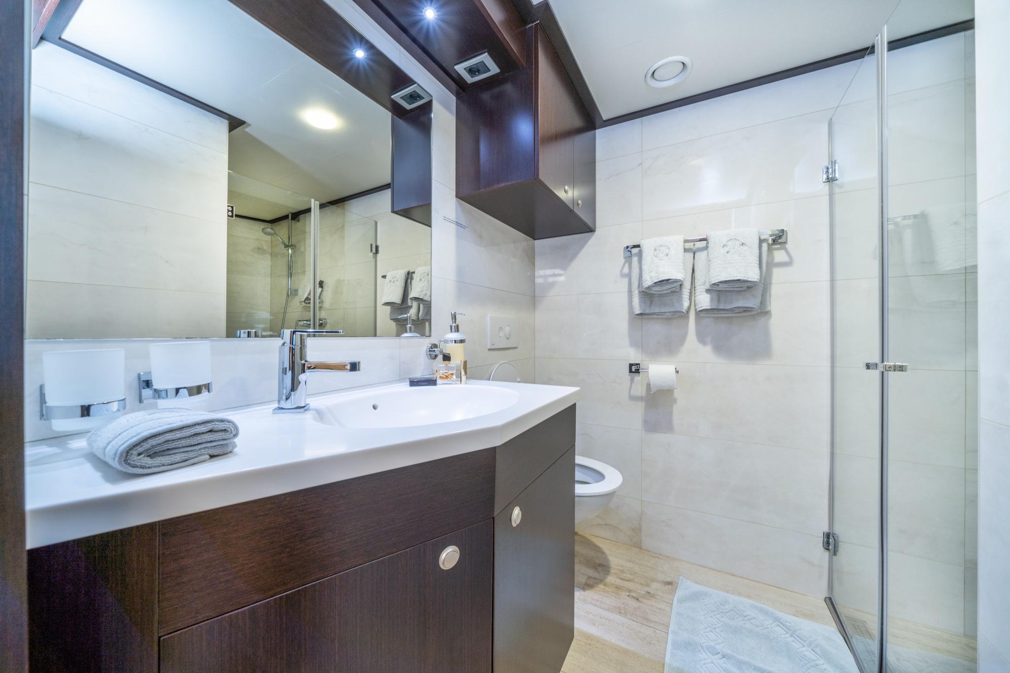 luxury yacht bathroom featuring white marble walls, glass shower enclosure, and dark wood vanity