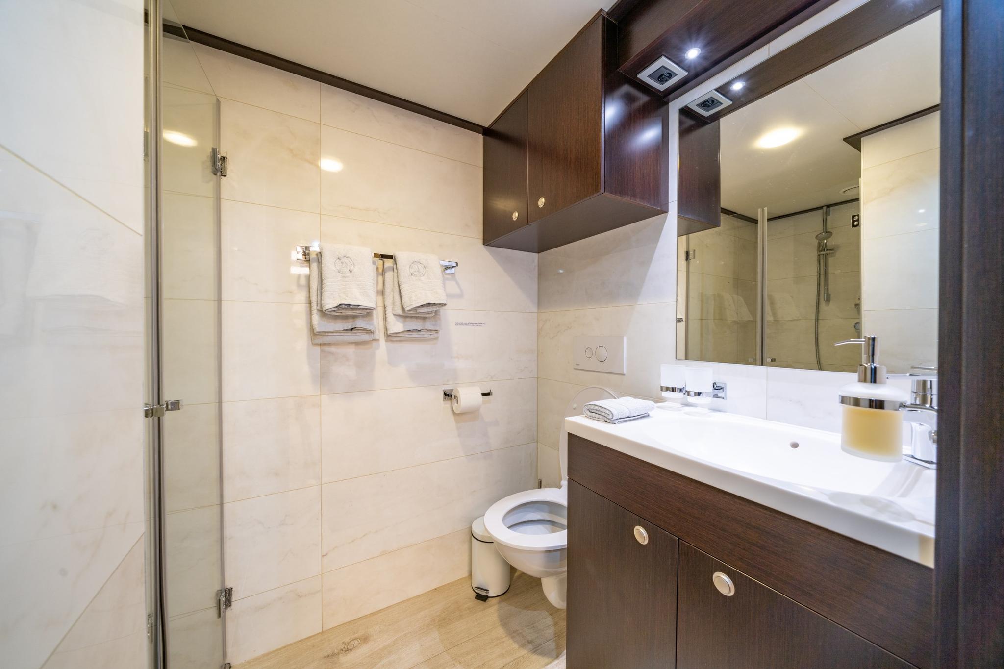 yacht bathroom featuring glass shower enclosure, white toilet, dark wood vanity with white countertop