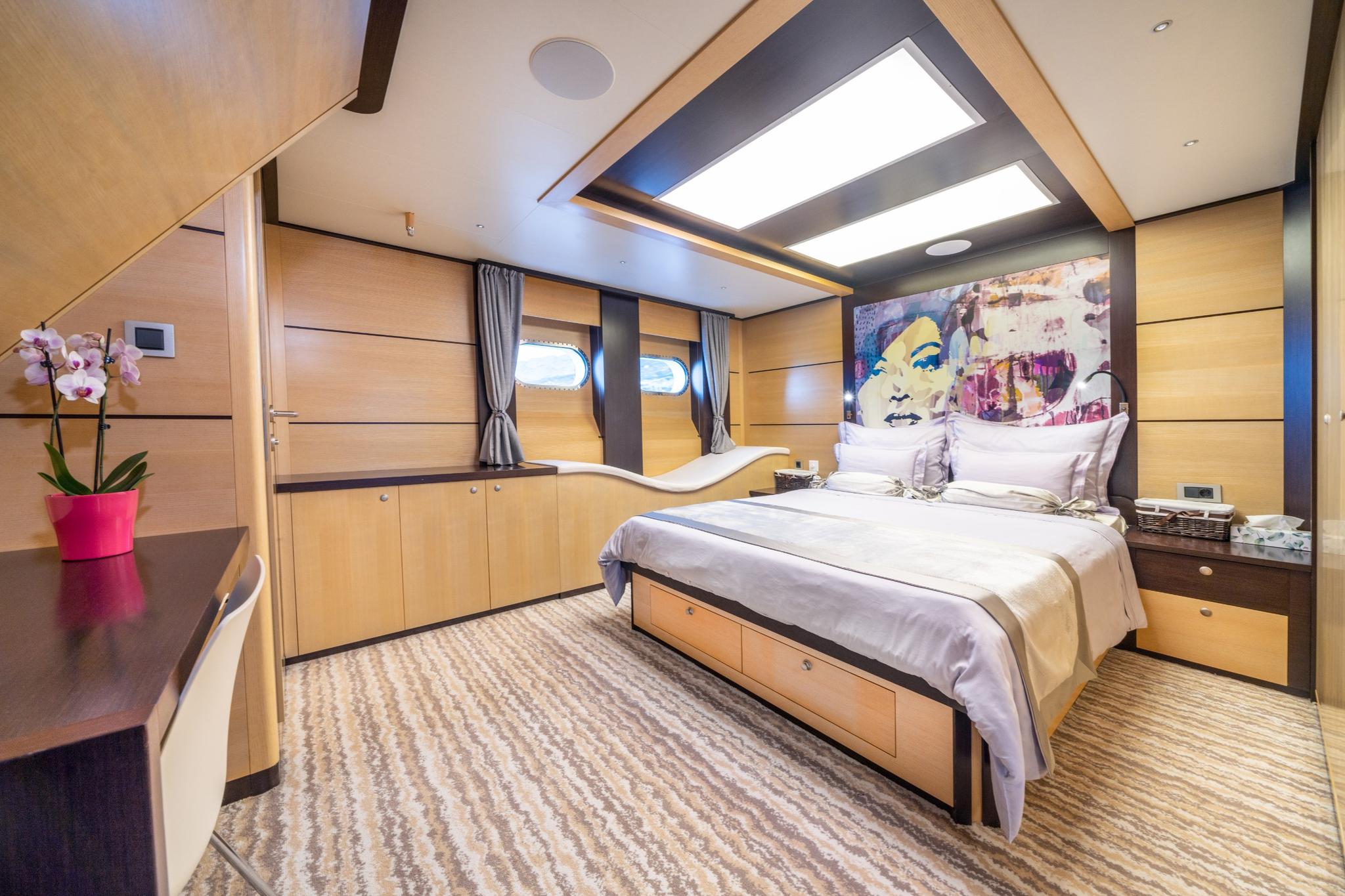 luxury yacht master cabin featuring double bed, wood paneling, portholes with curtains, and colorful artwork
