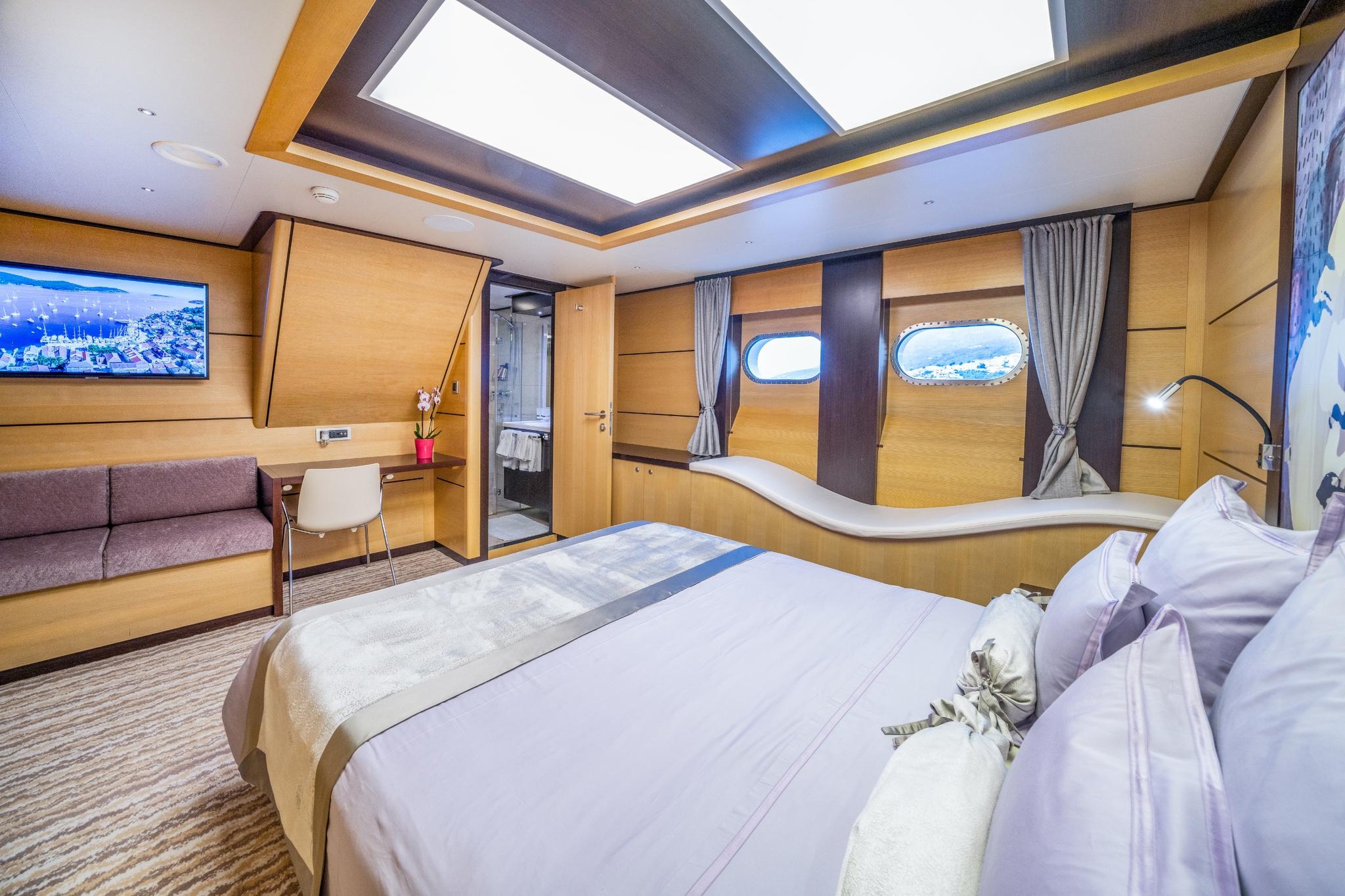luxury yacht master cabin featuring king bed, panoramic oval windows, ensuite bathroom entrance and built-in sofa