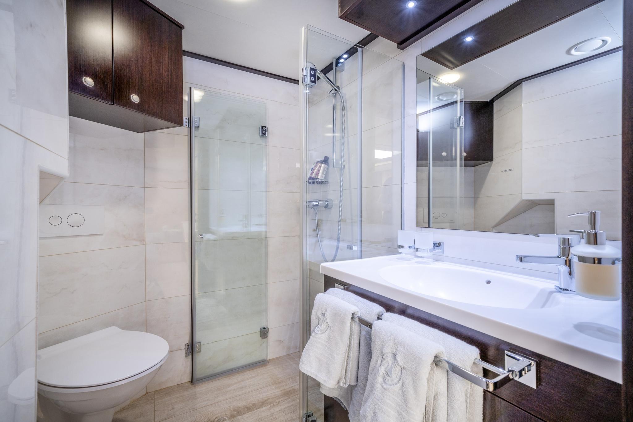 luxury yacht bathroom featuring glass shower enclosure, white vanity with dual sinks and mirror