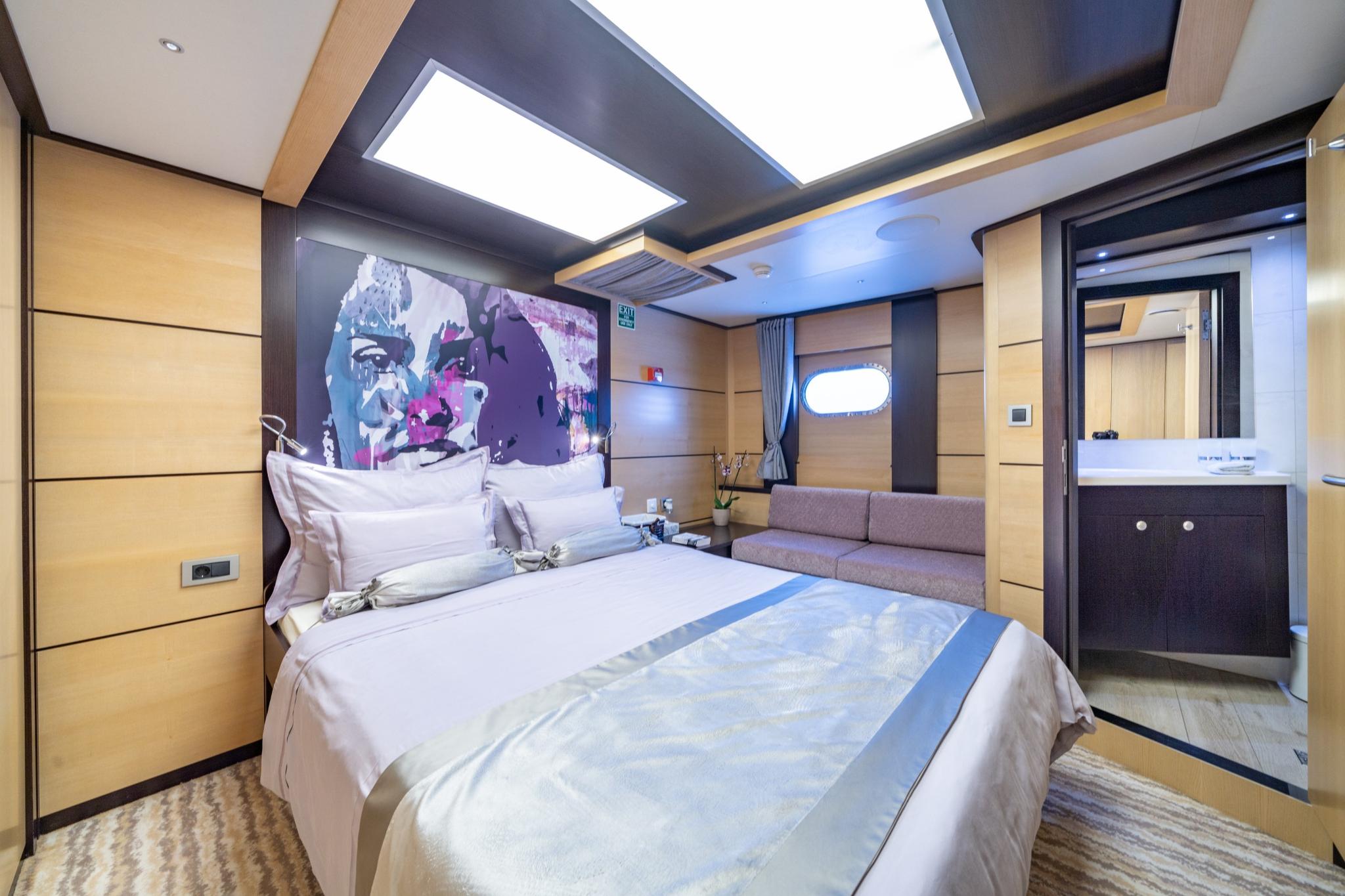 luxury yacht master cabin with double bed, built-in seating, colorful artwork and ensuite bathroom entrance