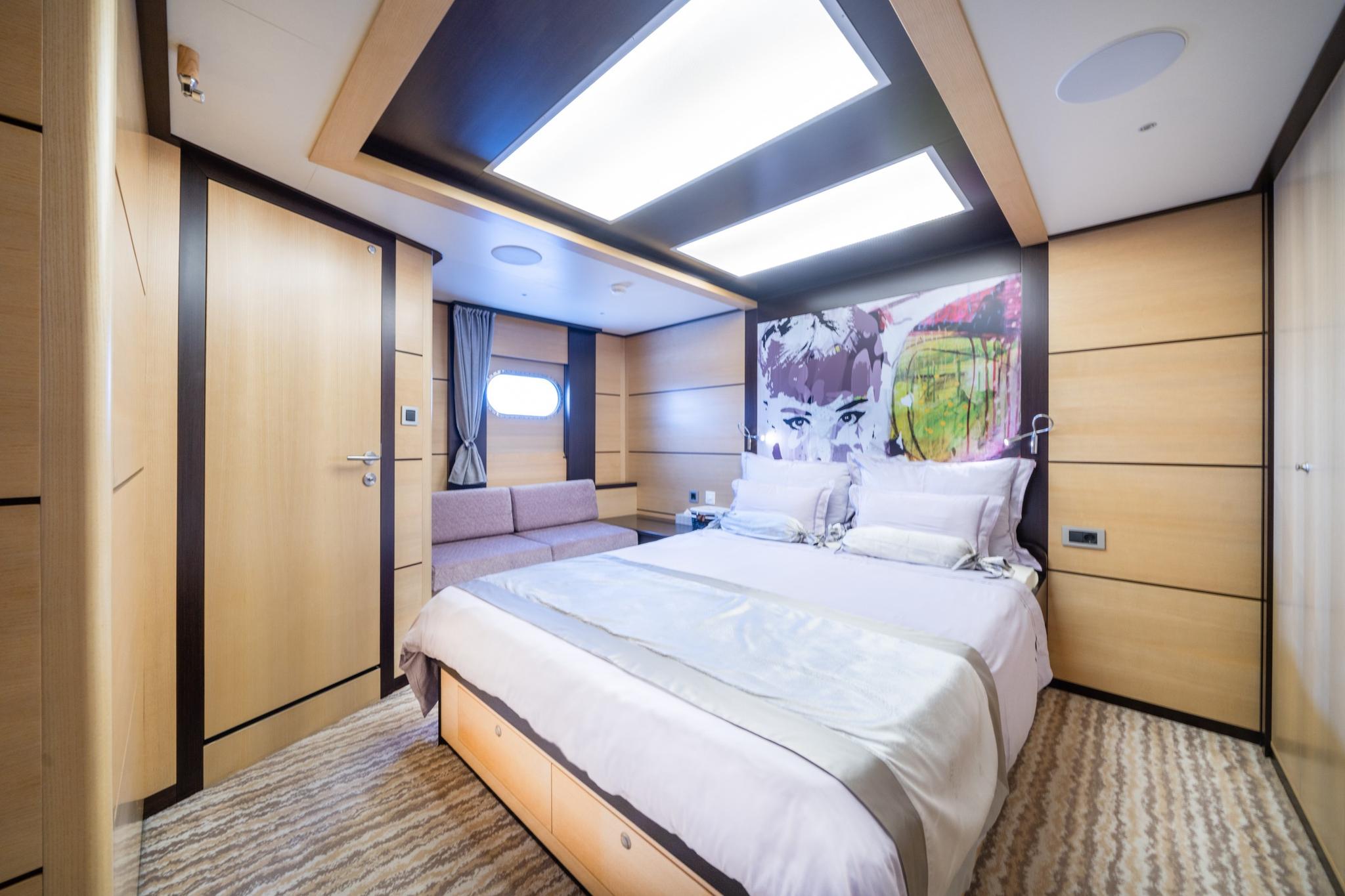 yacht guest cabin interior with double bed, light wood paneling and colorful wall art
