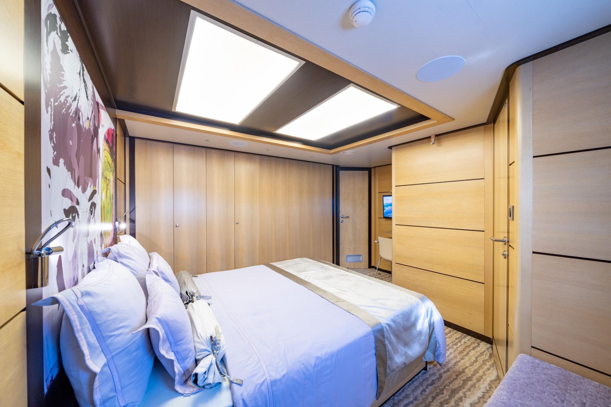 luxury yacht guest cabin featuring double bed with white linens and light wood wardrobes