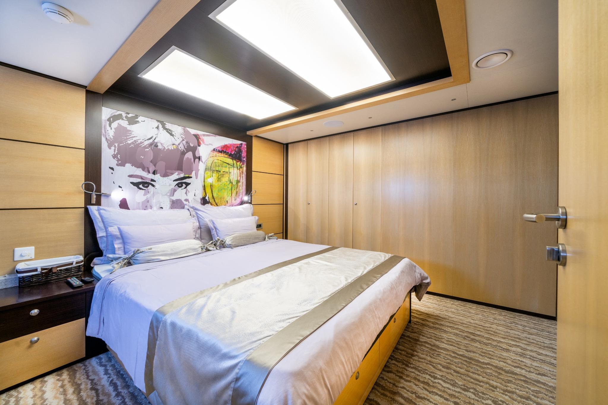 modern yacht cabin with double bed, colorful portrait artwork and wood-paneled wardrobes