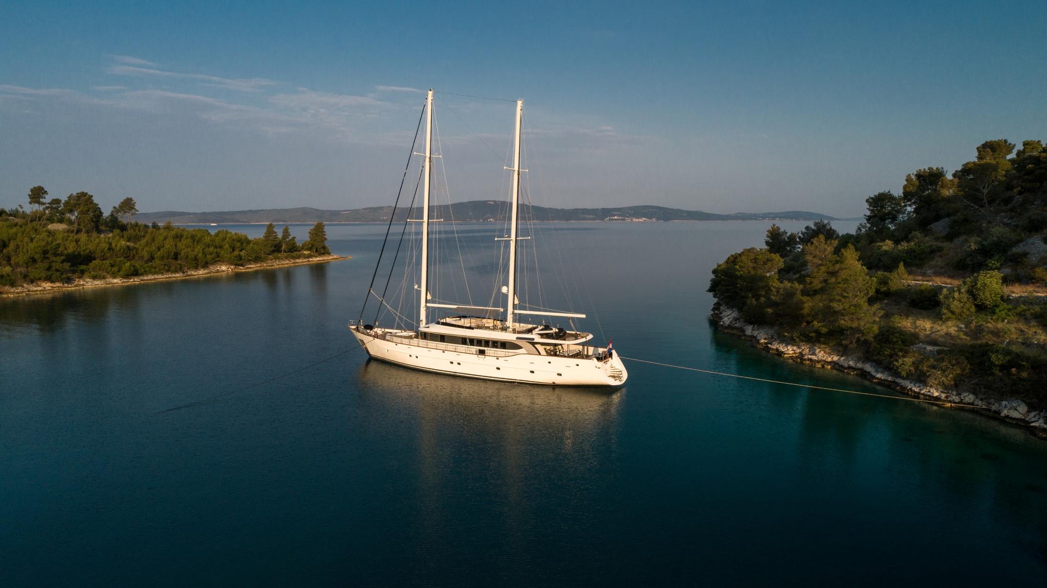 aerial view of white sailing yacht anchored in protected turquoise bay surrounded by green coastline