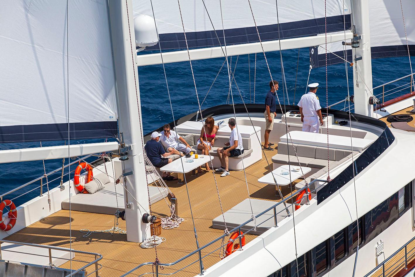 gulet main deck with white seating area, guests relaxing, crew members, teak decking