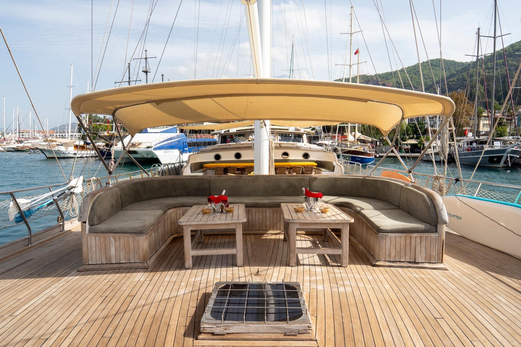 gulet aft deck with curved cushioned seating, teak tables and bimini shade cover