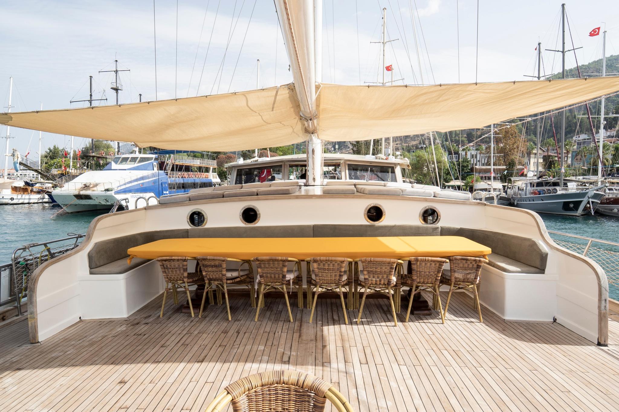 Gulet aft deck dining area with wicker chairs around table under beige awning
