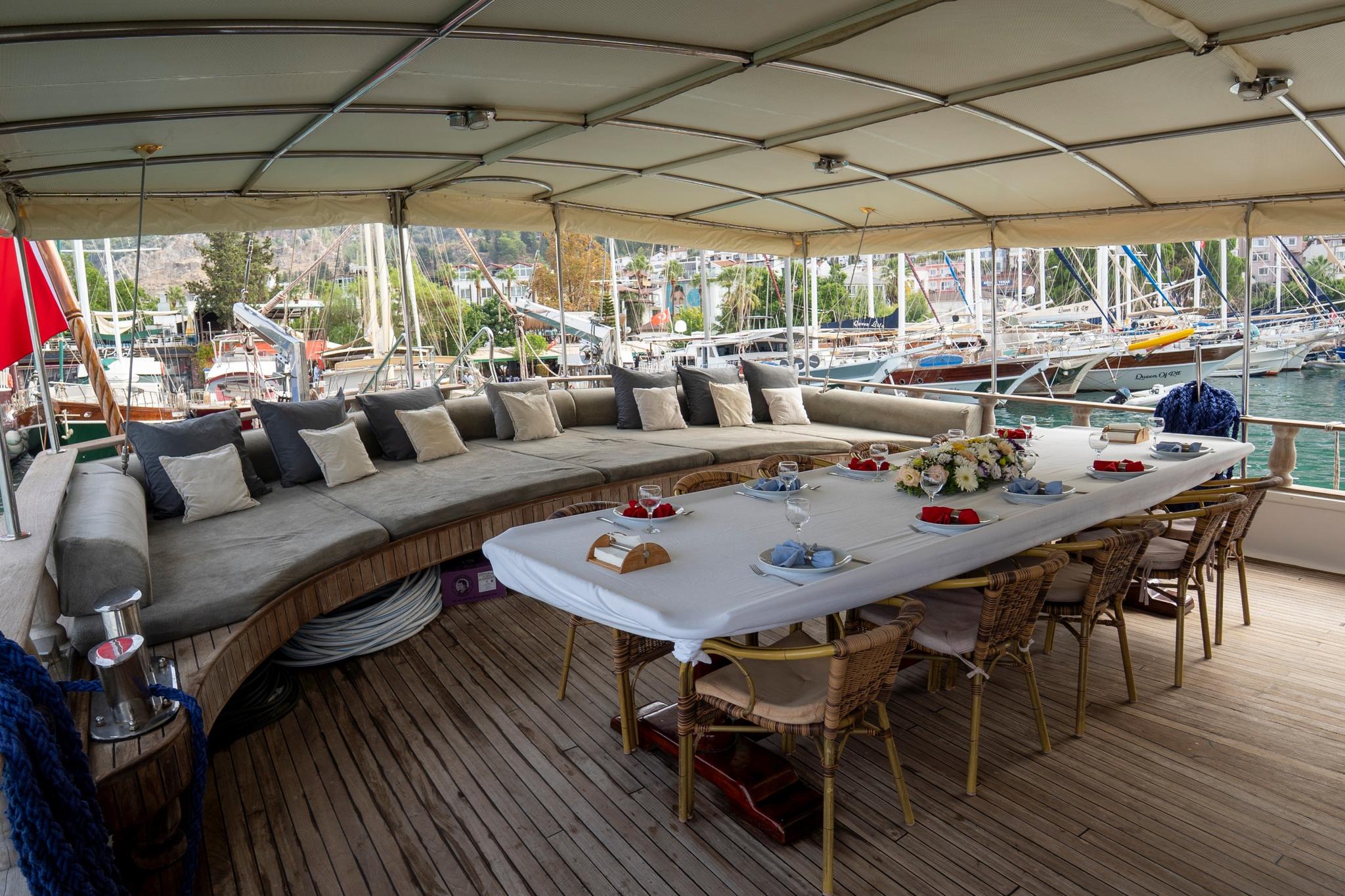 covered aft deck with white dining table, wicker chairs, and built-in seating with cushions overlooking marina