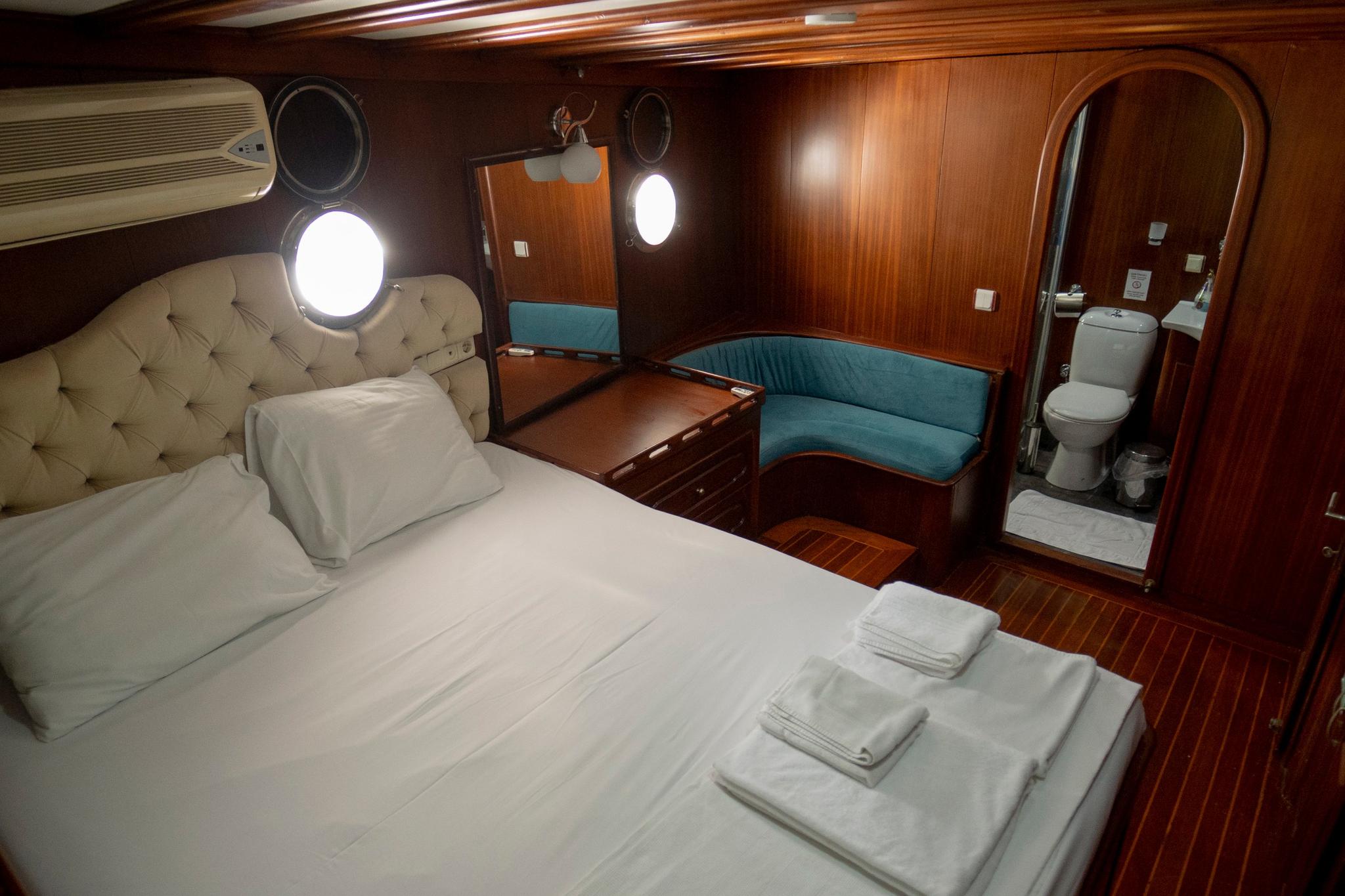 yacht cabin interior with double bed, teal seating area and en-suite bathroom visible