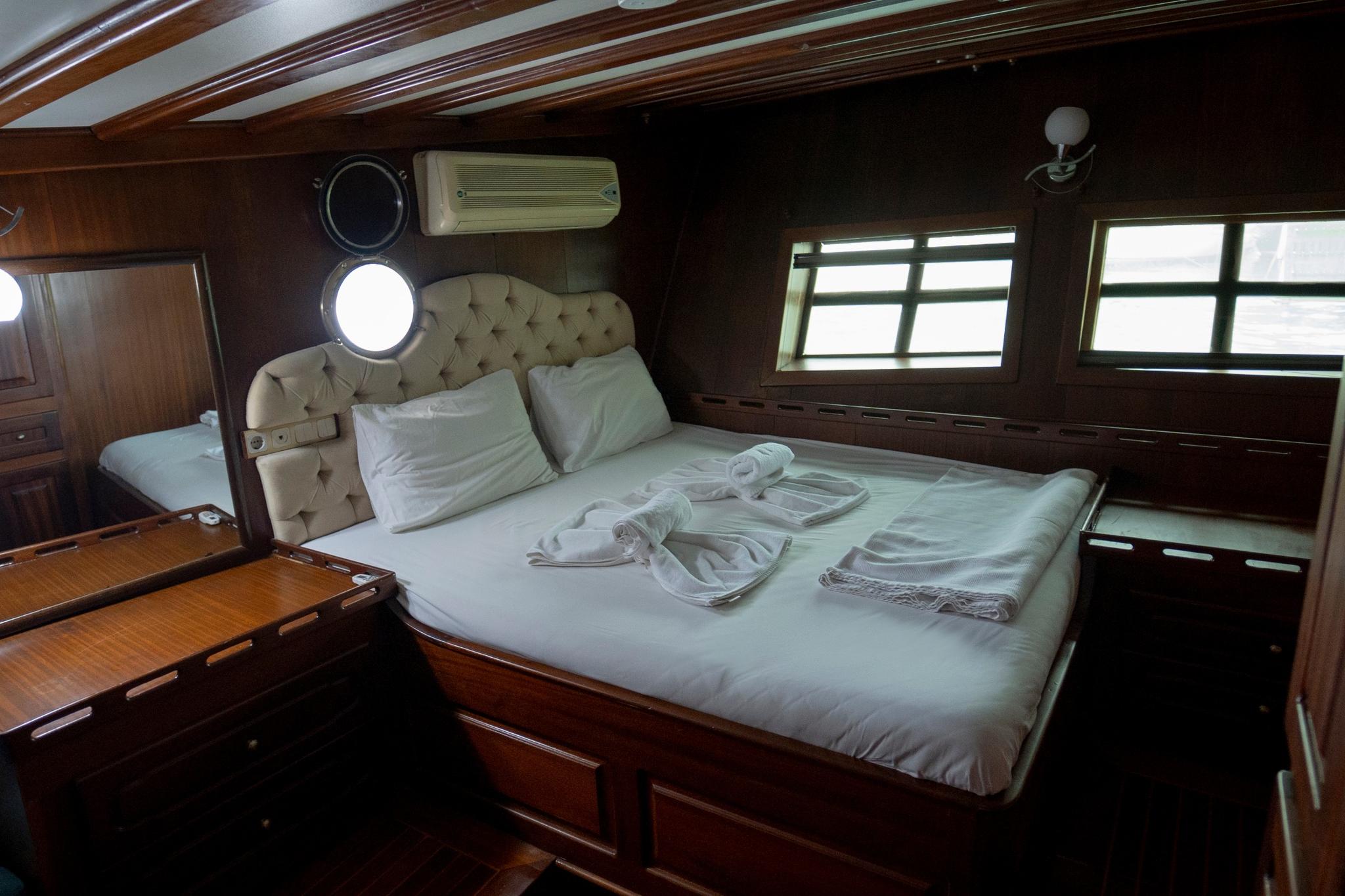 yacht cabin interior with double bed, tufted beige headboard, portholes and dark wood paneling