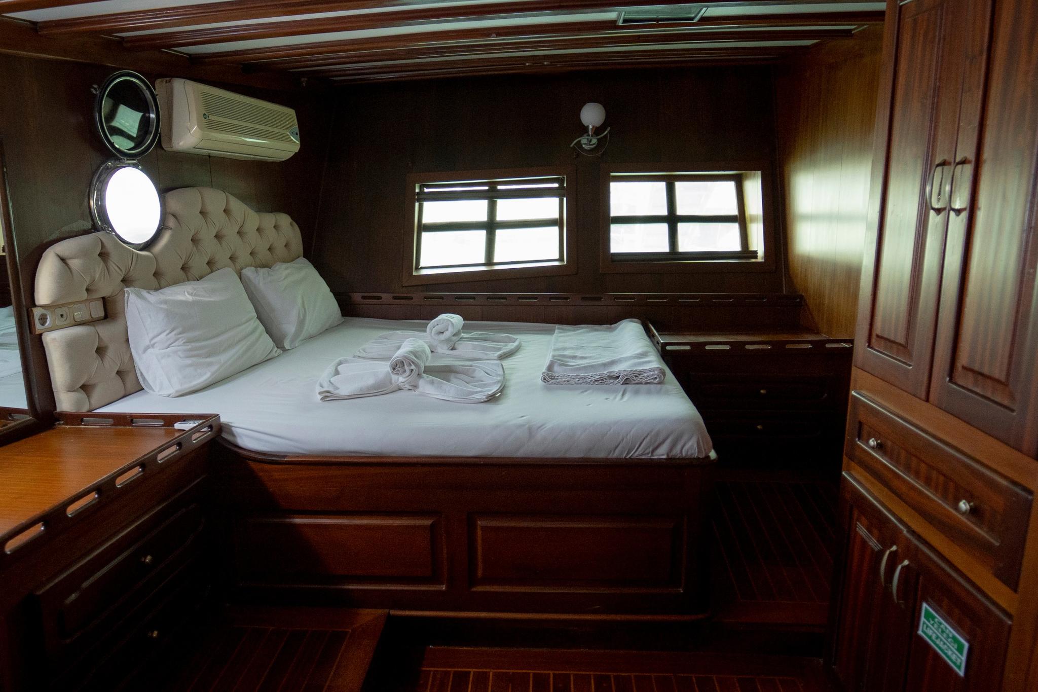 yacht guest cabin featuring double bed with tufted headboard and rich wooden cabinetry