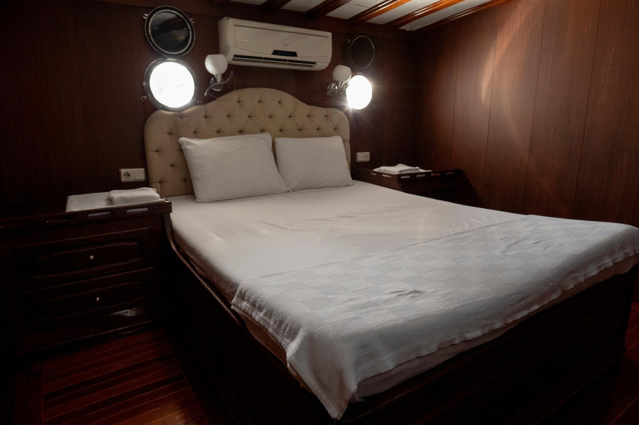 yacht cabin interior with double bed, beige tufted headboard, wooden paneling and air conditioning