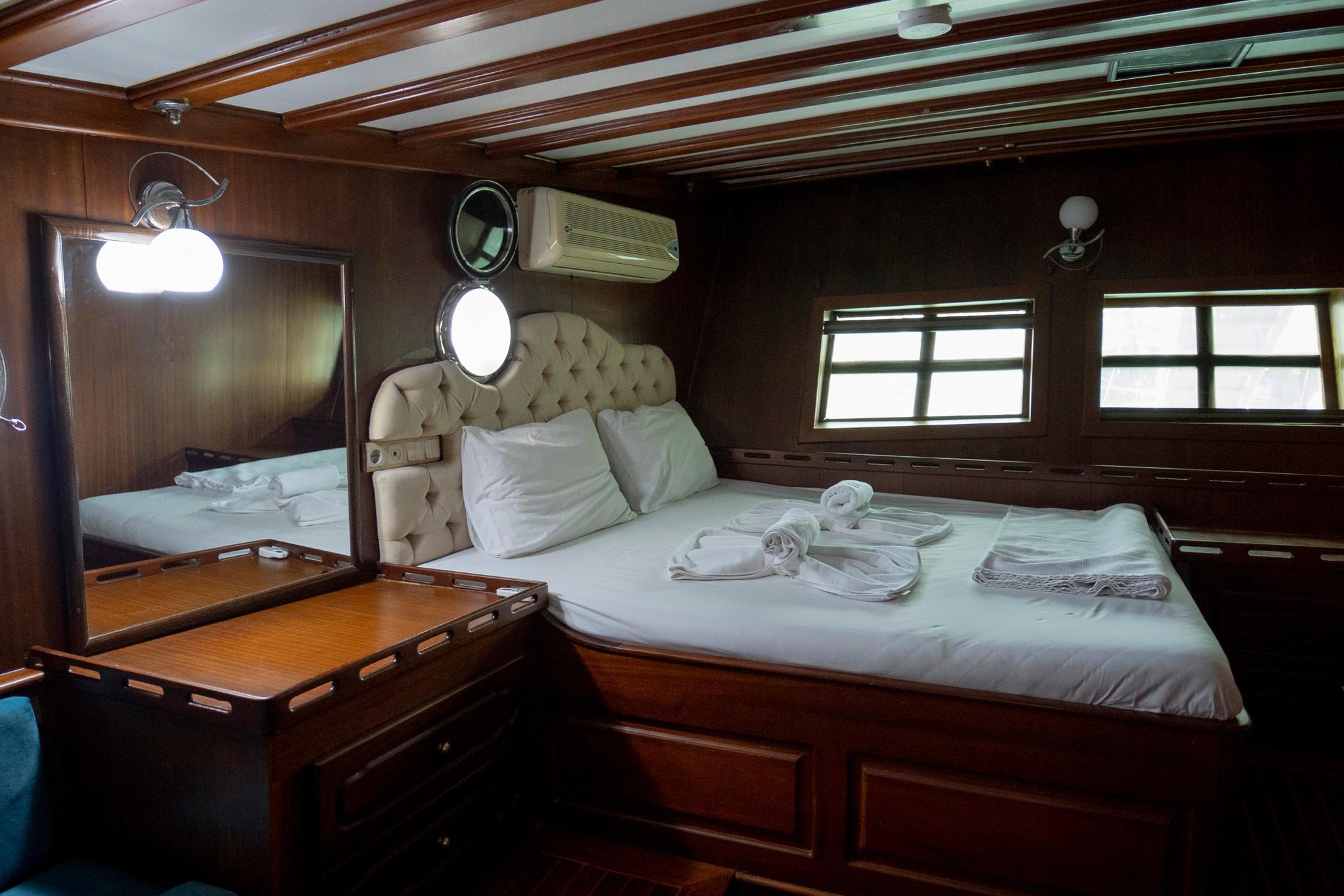 yacht guest cabin featuring double bed with beige tufted headboard and white linens