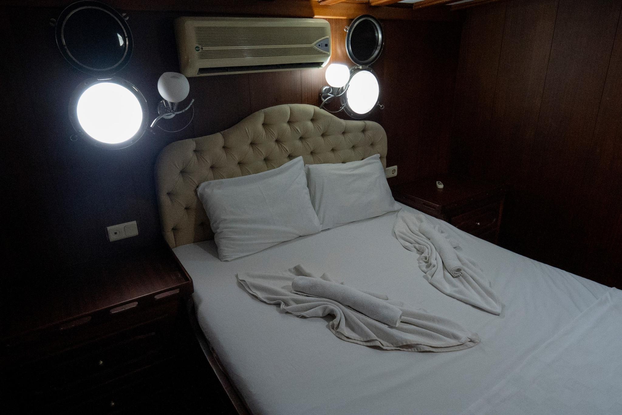 yacht guest cabin featuring double bed with beige tufted headboard and white linens