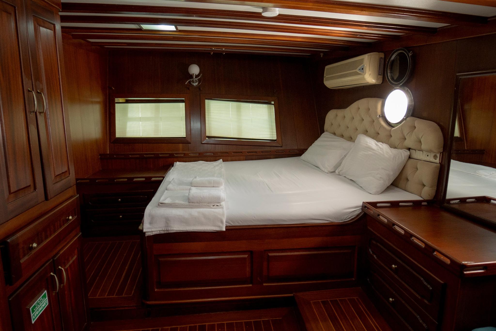 yacht guest cabin featuring double bed with white linens, beige tufted headboard, wooden paneling and portholes