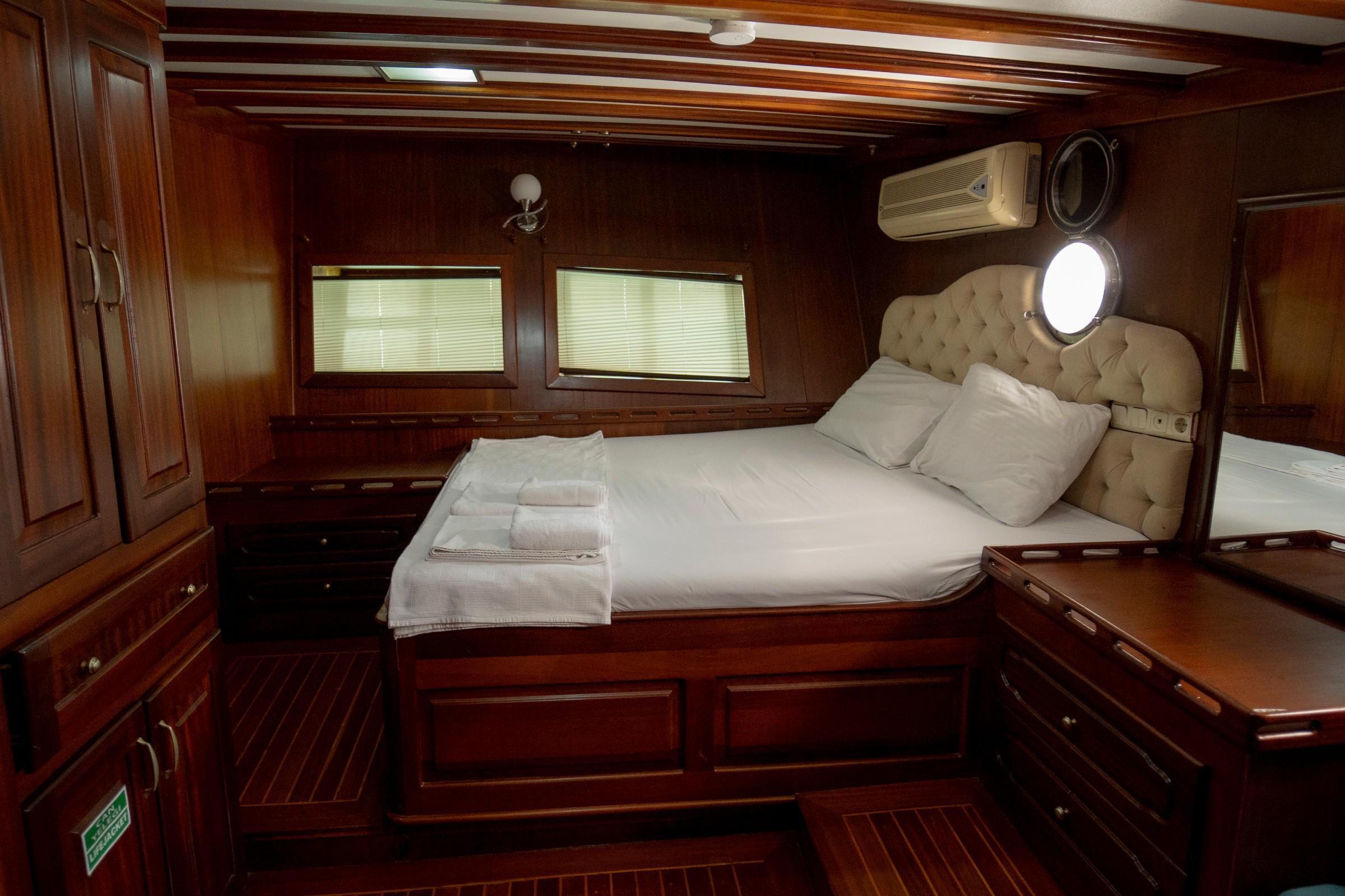 yacht guest cabin featuring double bed with white linens, beige tufted headboard, wooden paneling and portholes